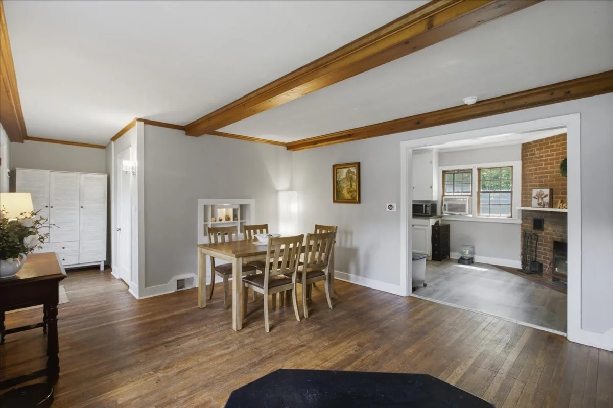 Home for sale with exposed ceiling beams showing dining area and large open entry into living and kitchen spaces.