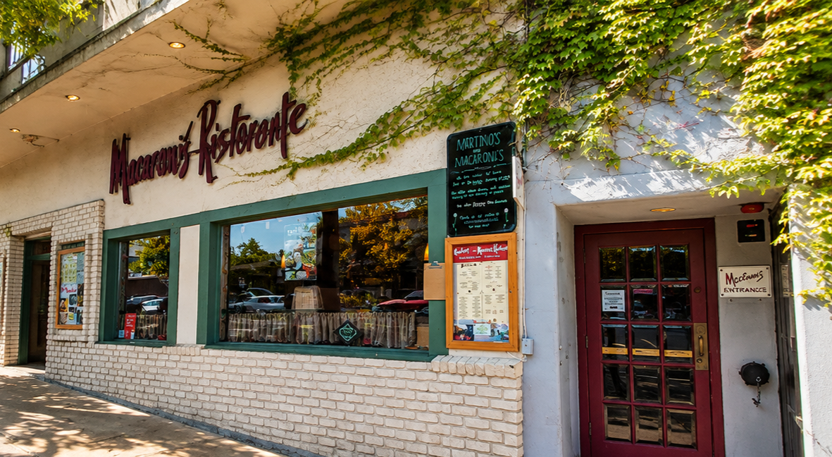 Exterior of Macaroons Ristorante with a brick facade, green window frames, and a maroon door. Signage indicates it serves macaroni and Italian dishes. There is a menu board outside and ivy growing on the wall.