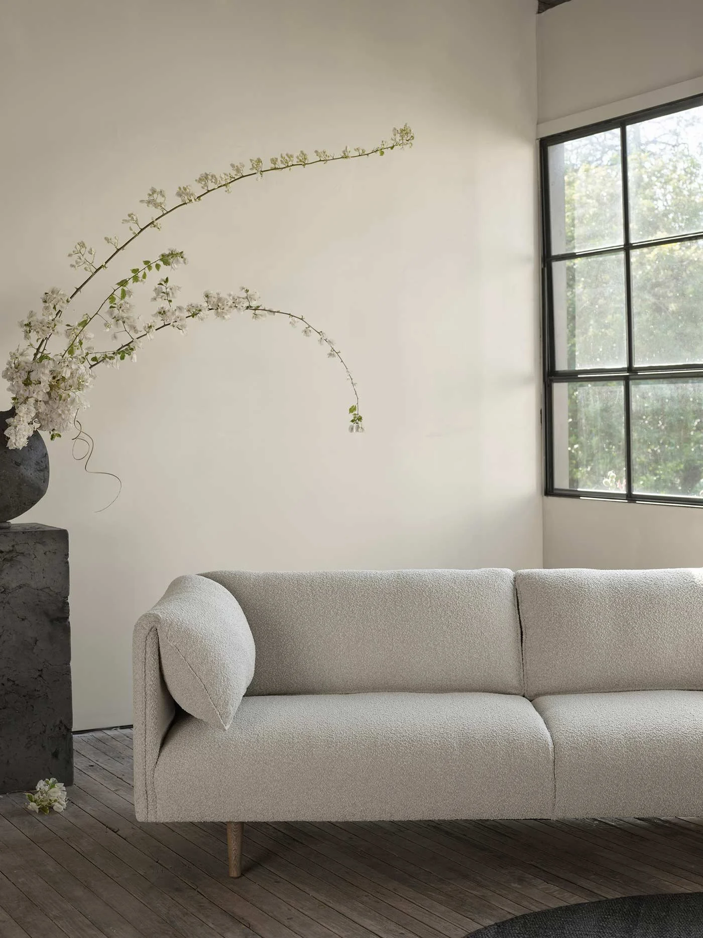 Comfy light warm grey sofa near a window and beautiful plant.