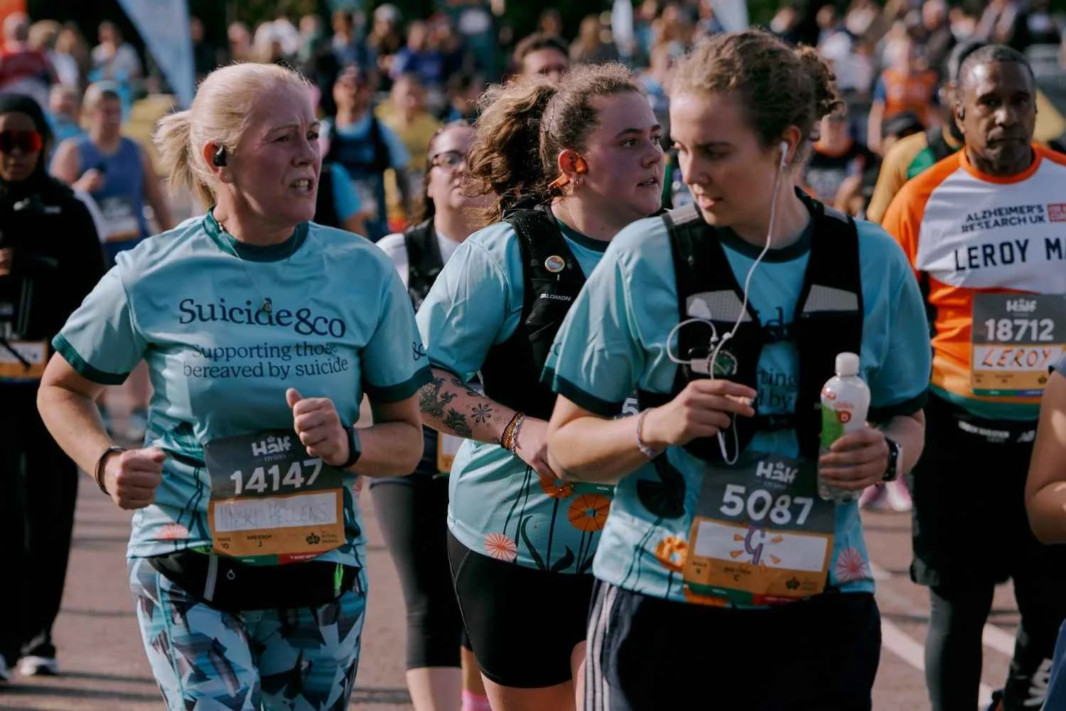 3 Suicide&Co Participants running a marathon outdoors on a city street, amongst a crowd of other runners