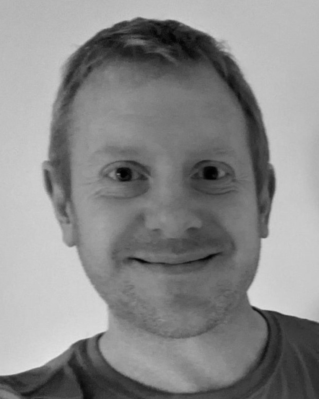 Black and white photo of a smiling man with short hair, wearing a striped shirt.