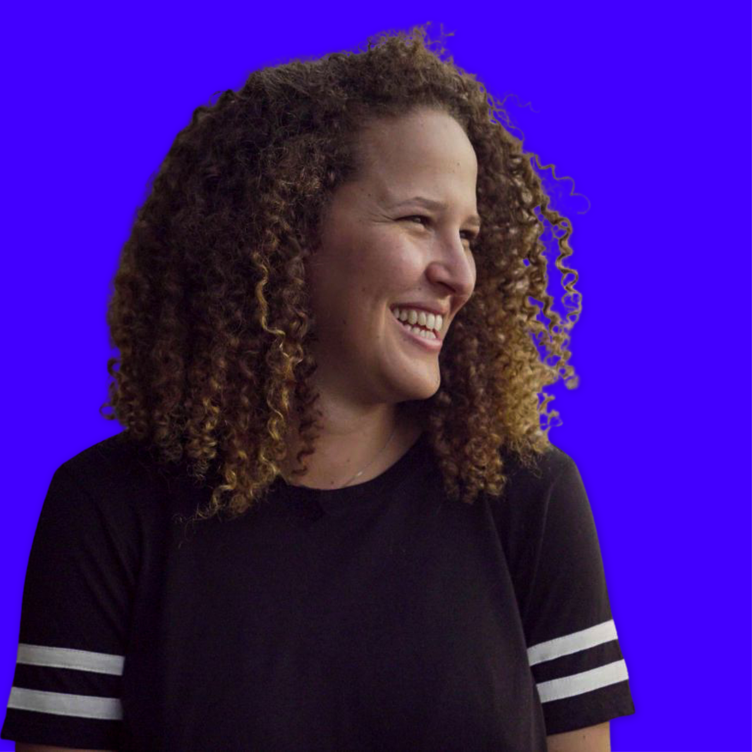 Portrait of a smiling woman with curly hair wearing a black t-shirt with white stripes on the sleeves, against a blue background.