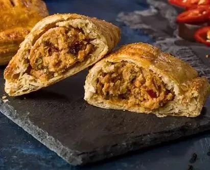 A sliced meat pie on a black surface with a flaky crust and meat filling.