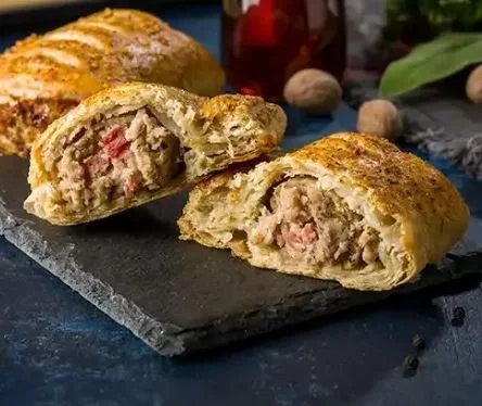 Cross-section of a golden baked pastry filled with ham and cheese, on a dark slate serving board.