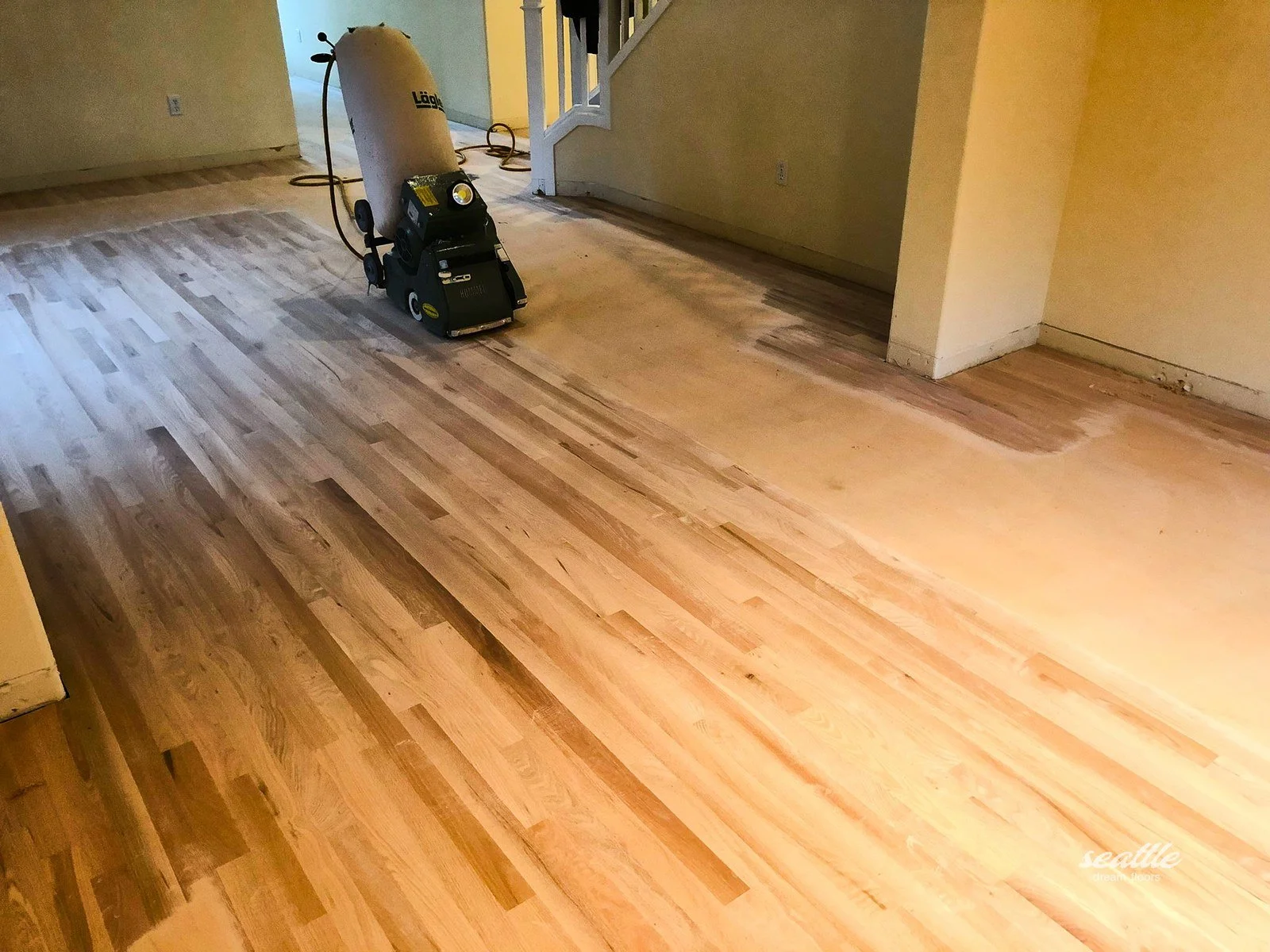 Floor sander with a dust bag on narrow boards partly sanded to bare wood