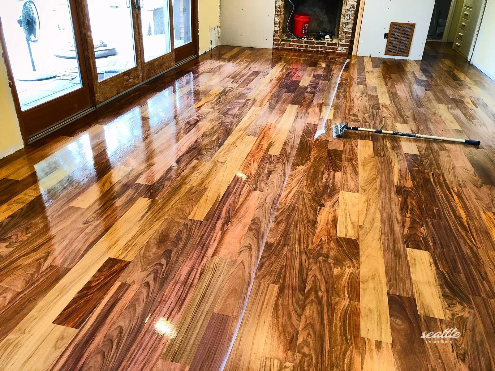 Wet finish coating half a floor of swirling mixed tone planks beside an applicator