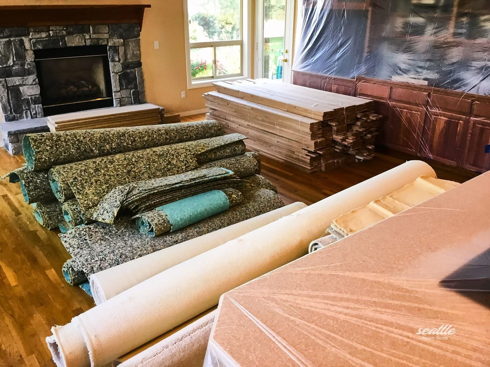 Removed carpet rolls beside a stack of new unfinished boards near a stone fireplace