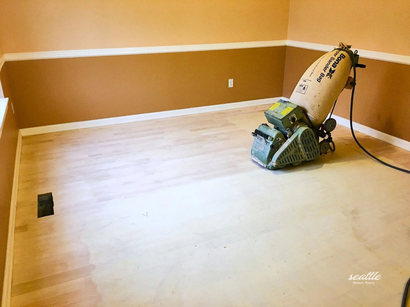 Green belt sander with a Bona dust bag on a freshly sanded pale strip floor