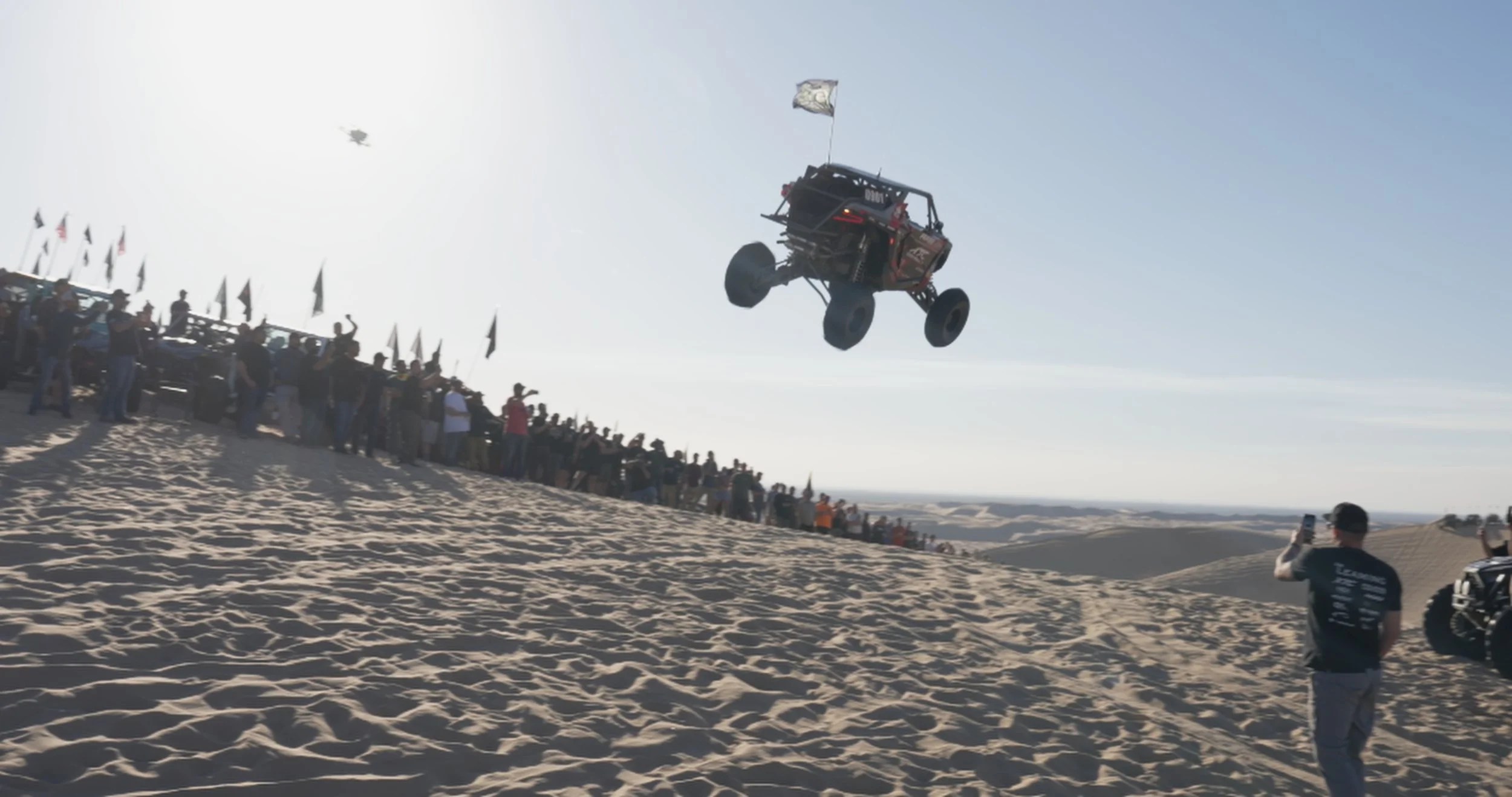 Off-road UTV jumping through the air in front of a crowd at a desert dunes gathering.