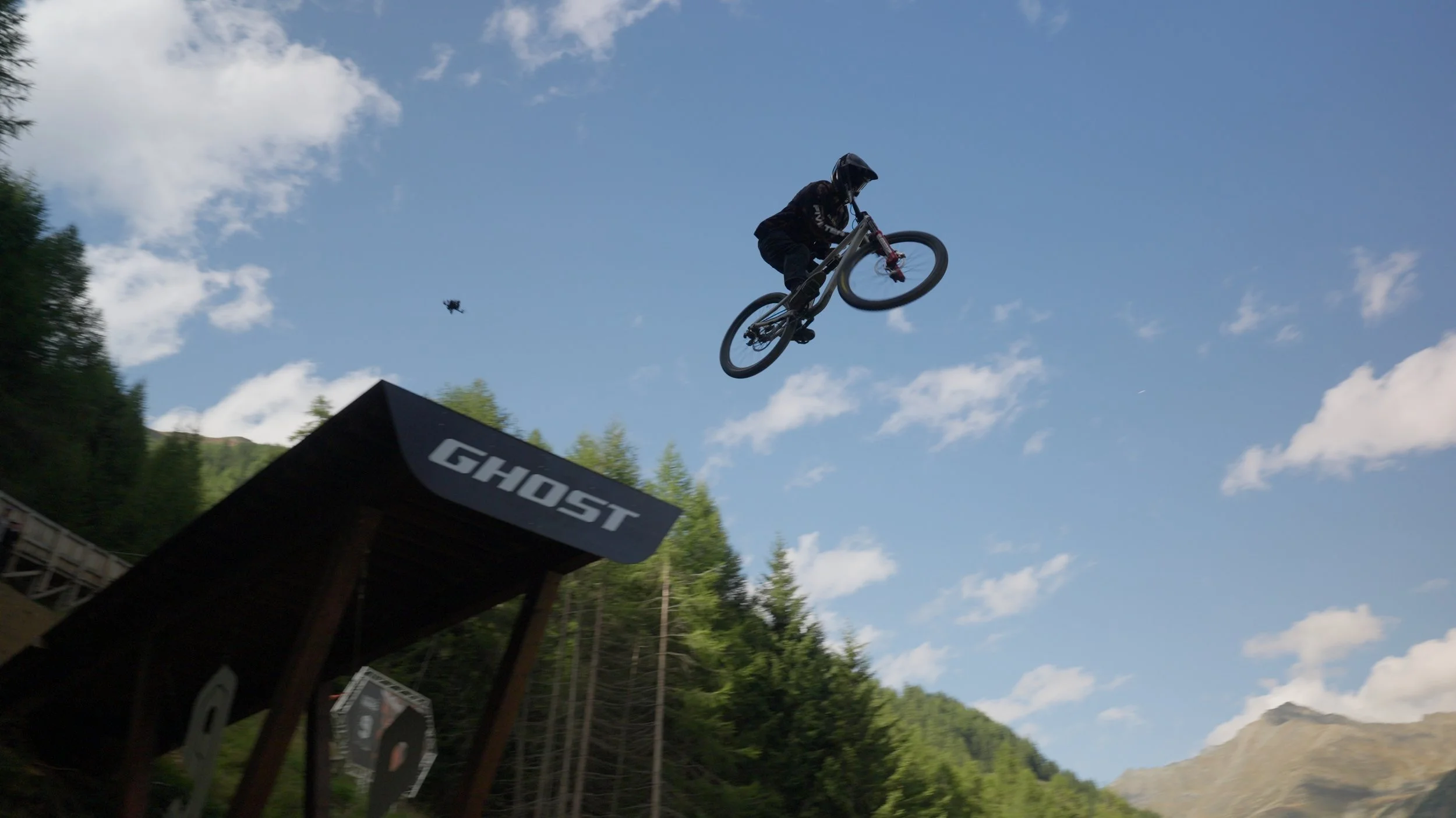 Mountain bike rider performing aerial trick over dirt jump during Swatch Nines Austria, captured using drone filming and high-speed tracking shots.