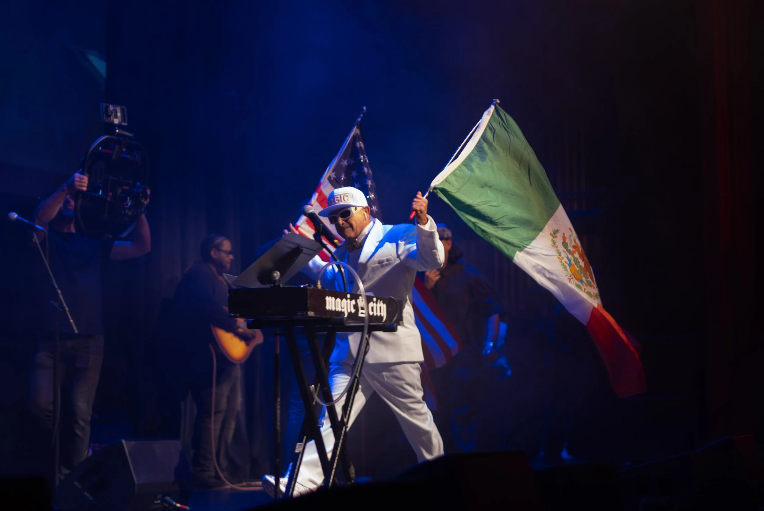 MC Magic performing on stage while holding Mexican and American flags during the 30 Years of Magic live concert