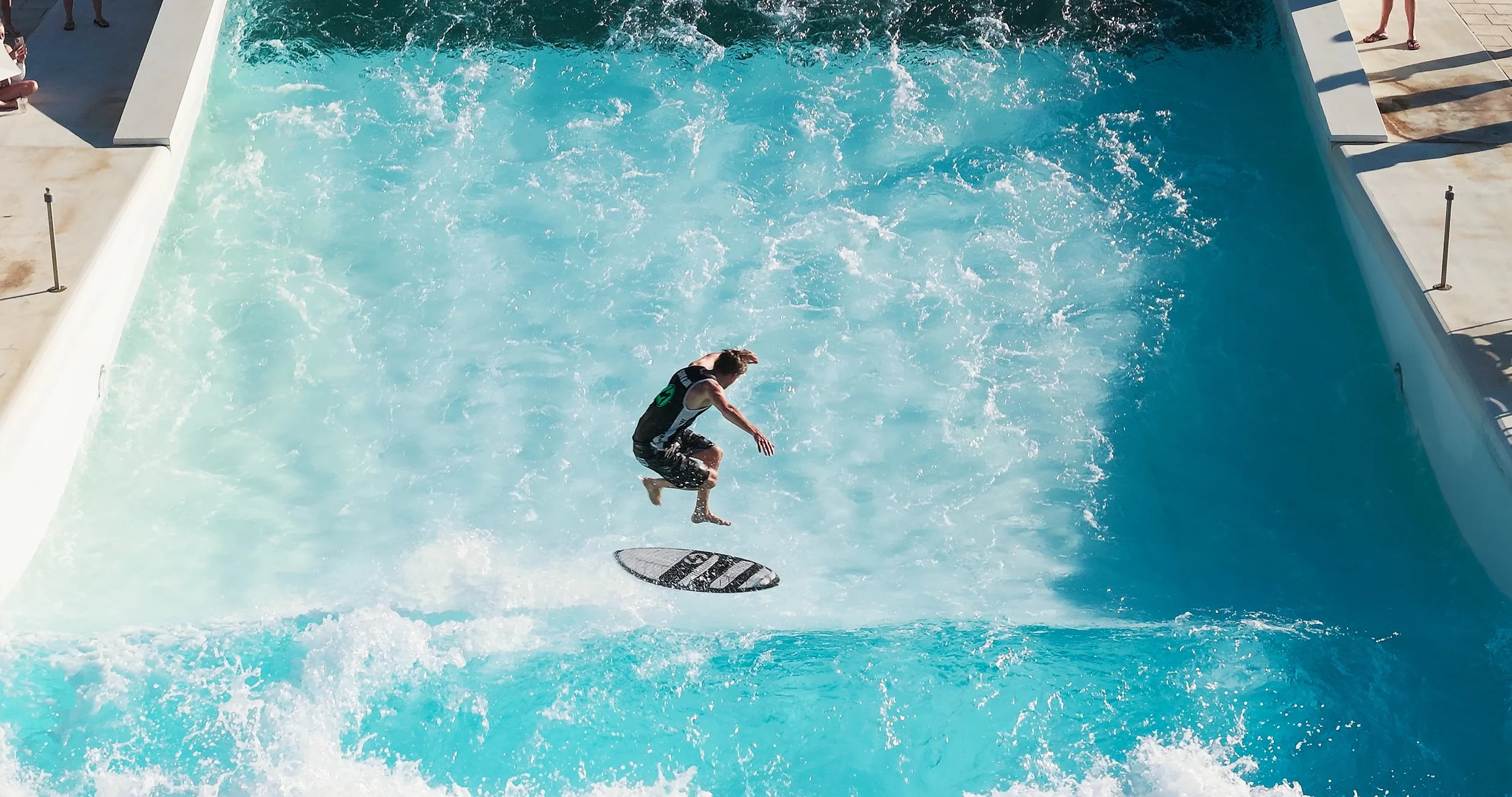 Person surfing a wave on a flowboarding pool, mid-air, at a water park.