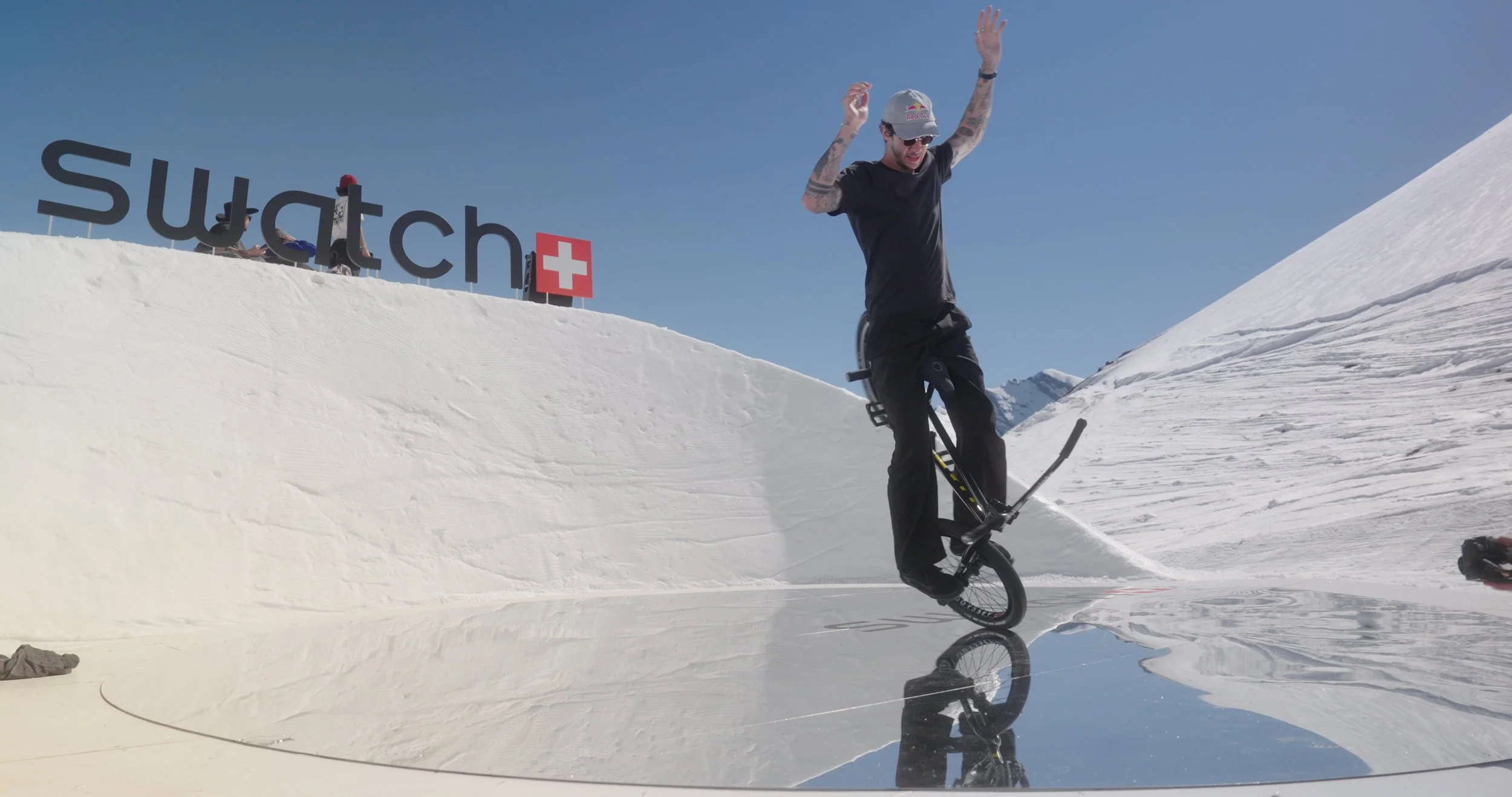 Flatland BMX athlete spinning on custom-built snow feature during Swatch Nines Switzerland event, filmed as part of live snowboard event production coverage.
