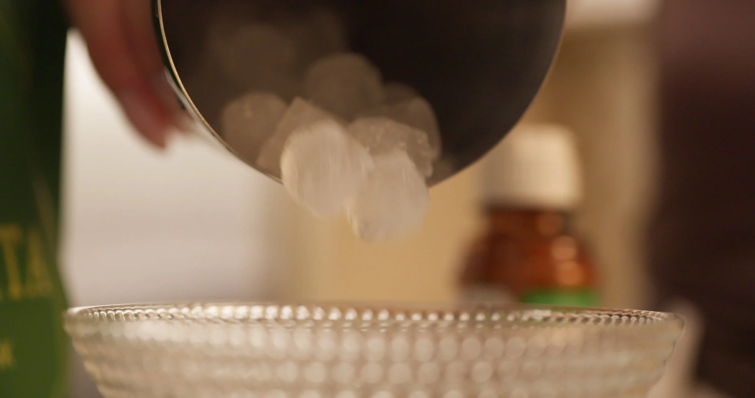 Adding ice cubes from a metal container into a glass bowl.