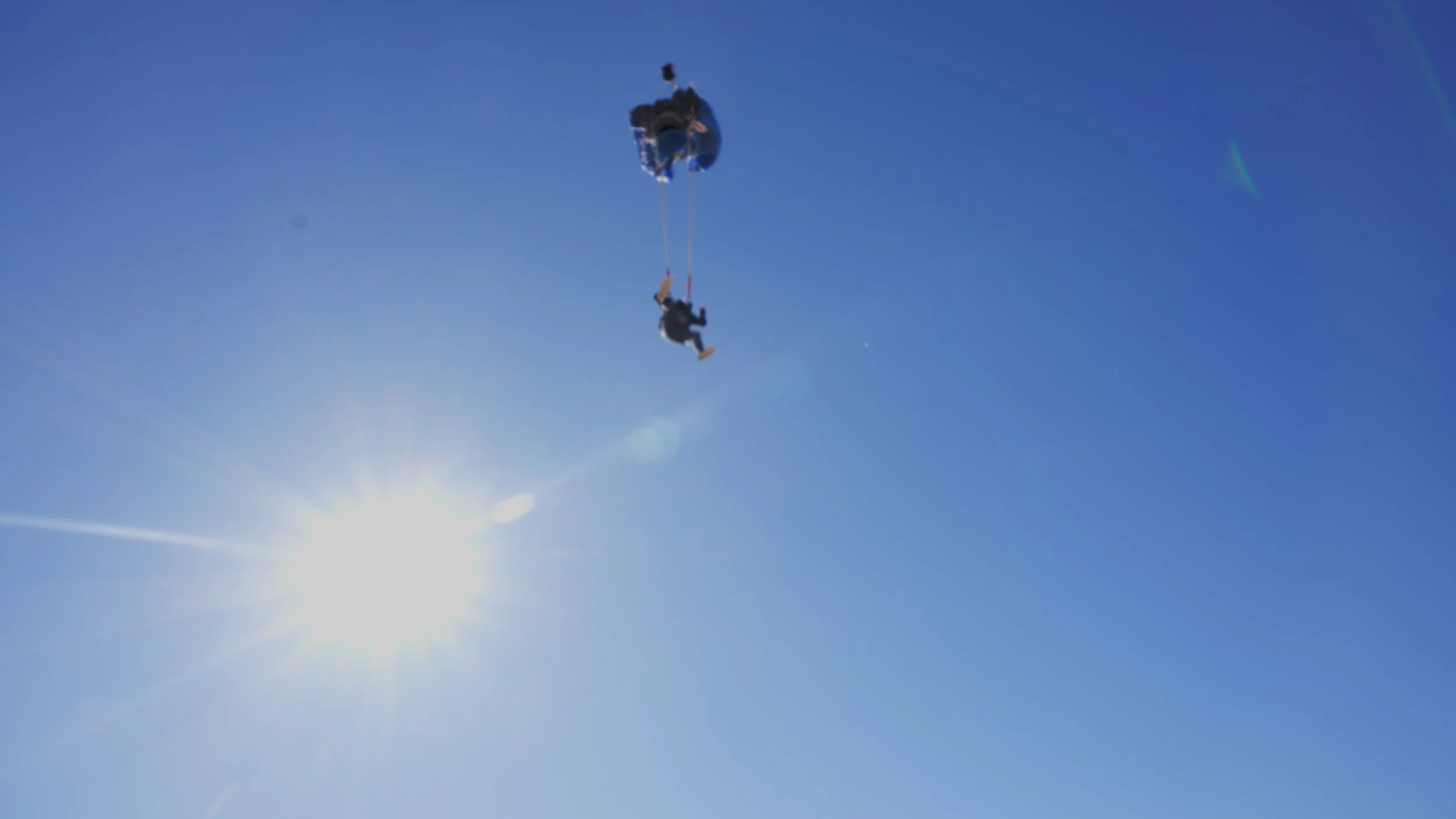 Person riding a longboard attached to a parasail in the clear blue sky with the sun shining brightly.
