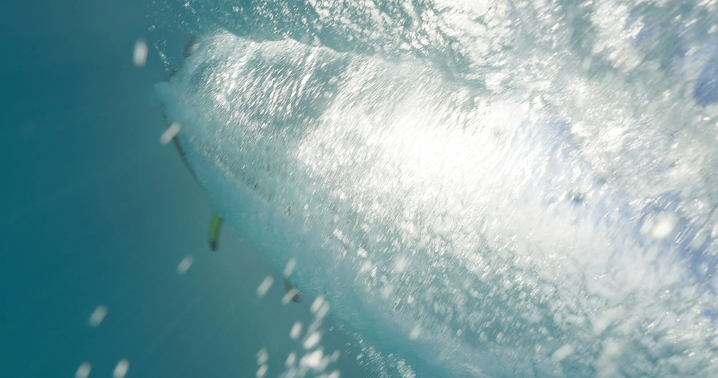 Underwater view of a surfboard riding a wave with sunlight filtering through the water.