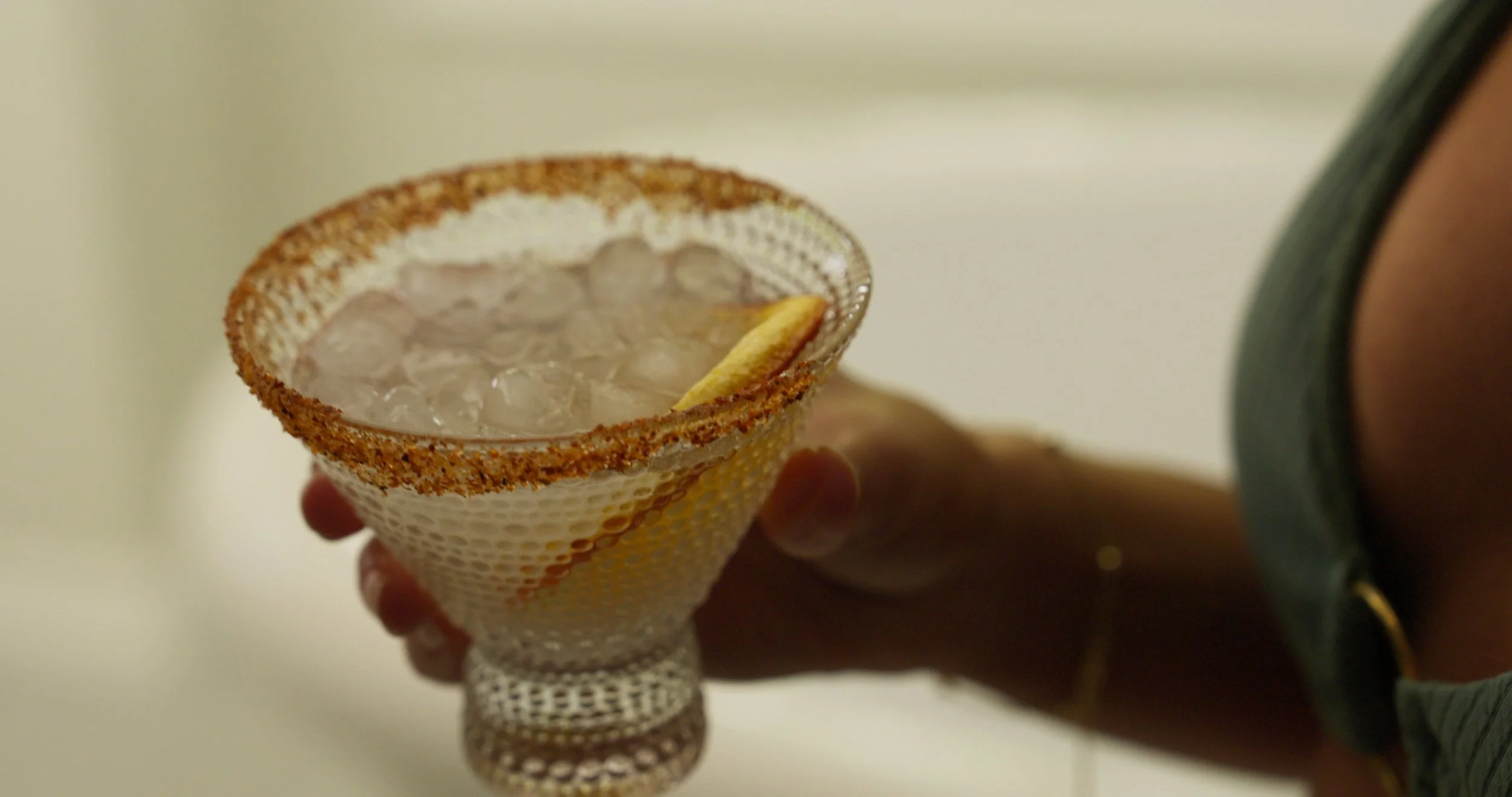 A hand holding a cocktail glass with a salted rim, filled with ice and a lime wedge