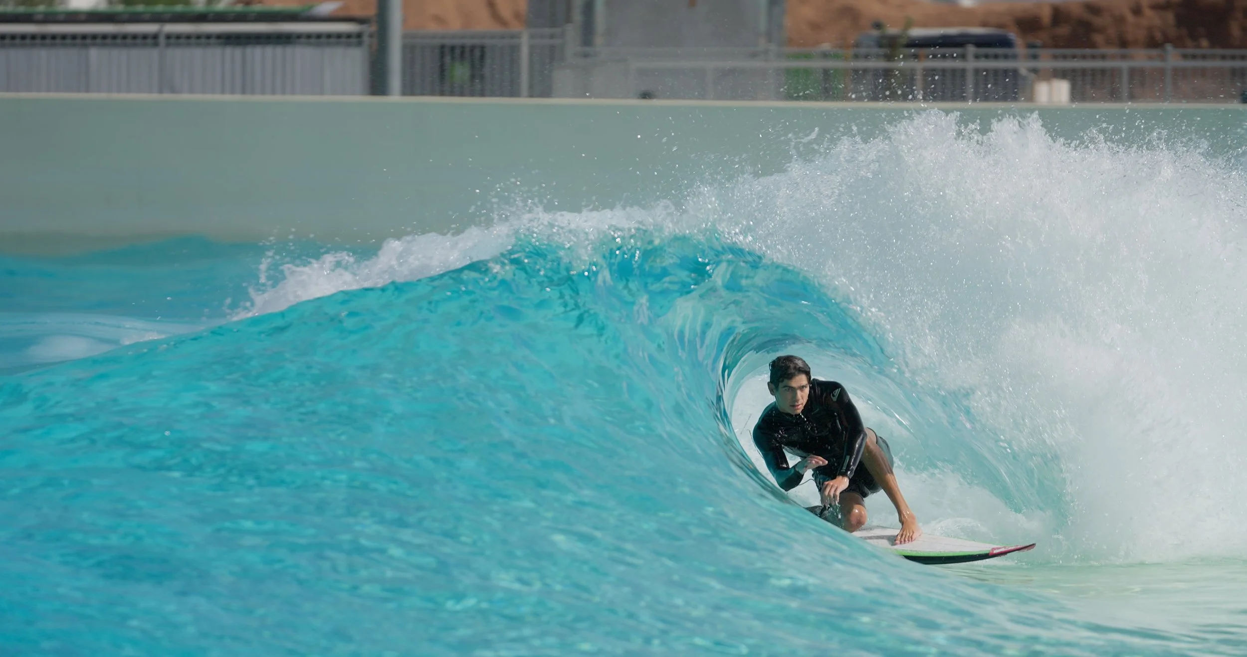 A young man surfing inside a large turquoise wave at an outdoor surf park.