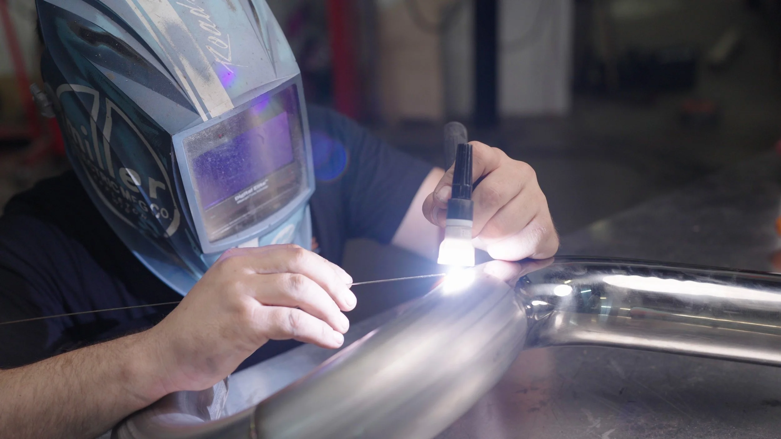 Custom car builder welding a performance exhaust component during production for the Barrett-Jackson Cup documentary series.