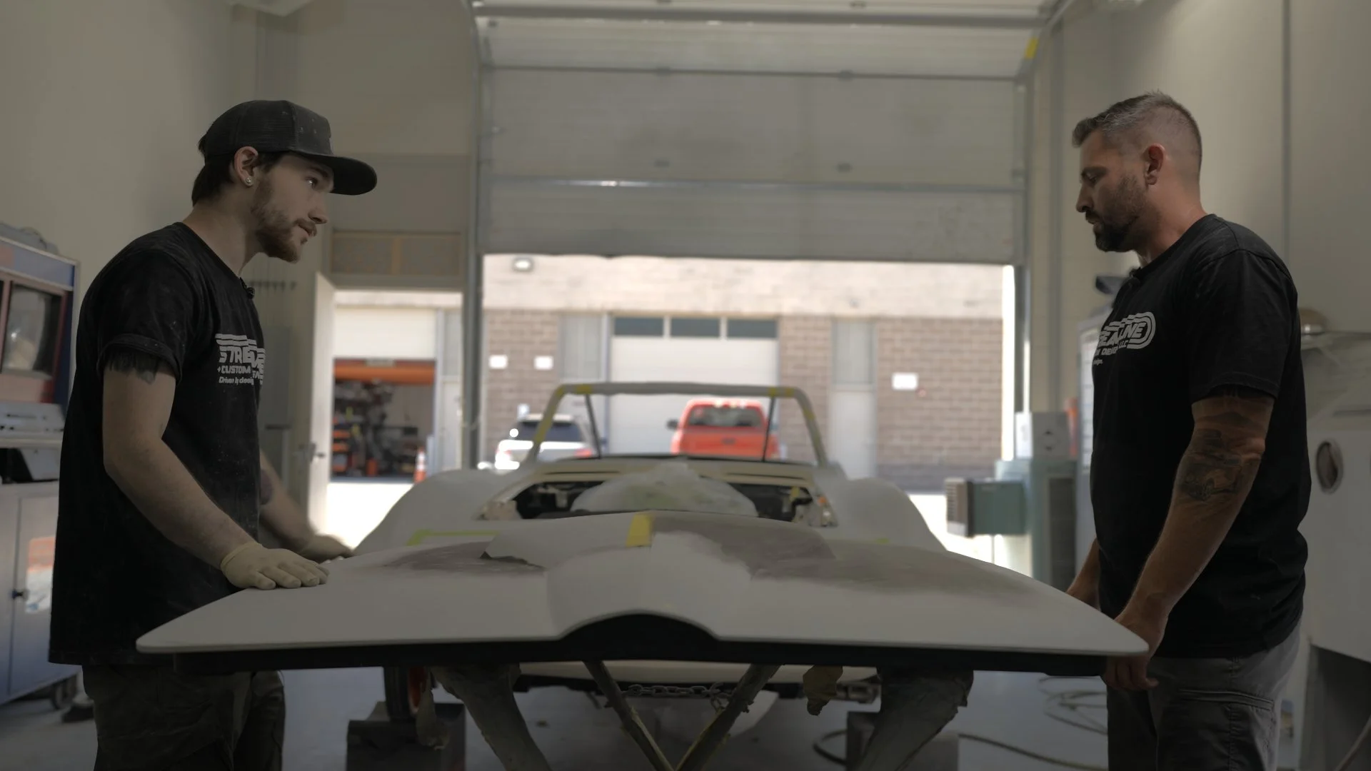 Streamline builders reviewing custom body panel modifications inside Salt Lake City performance shop during Barrett-Jackson Cup build