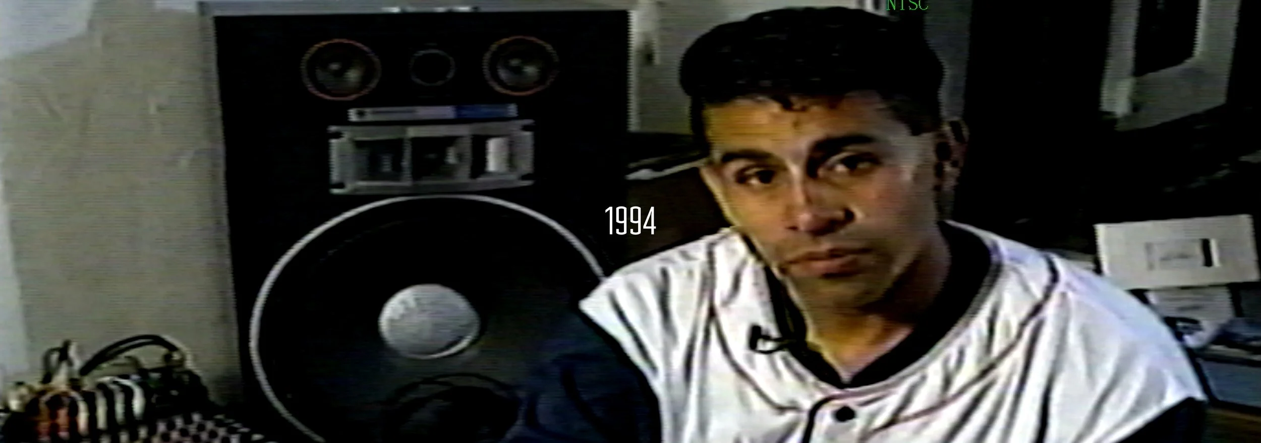 A young man wearing a baseball jersey sitting in front of a large black boombox, with the year 1994 displayed in the center.