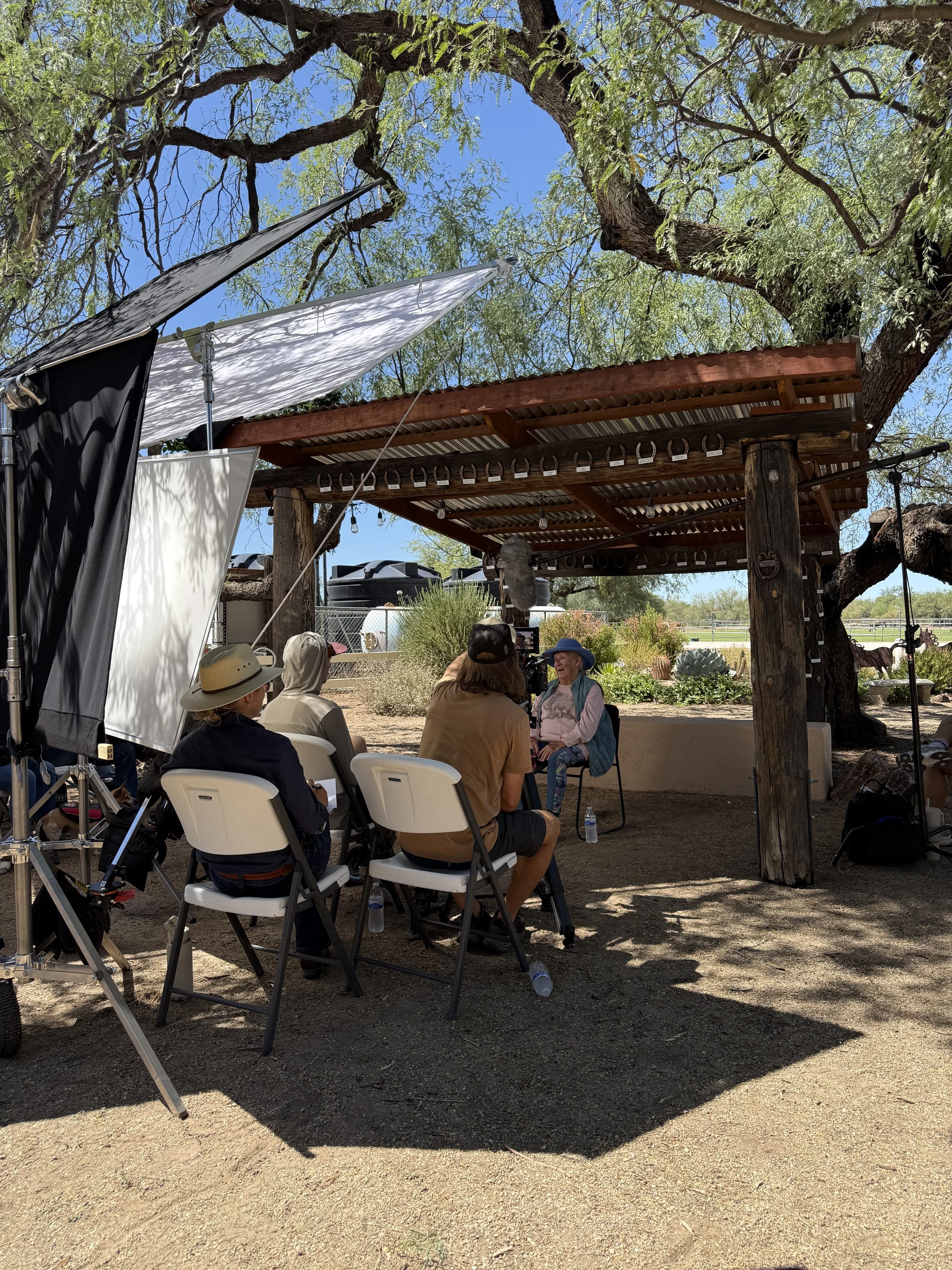 Outdoor documentary interview being filmed at a ranch location with lighting, camera crew, and production equipment.