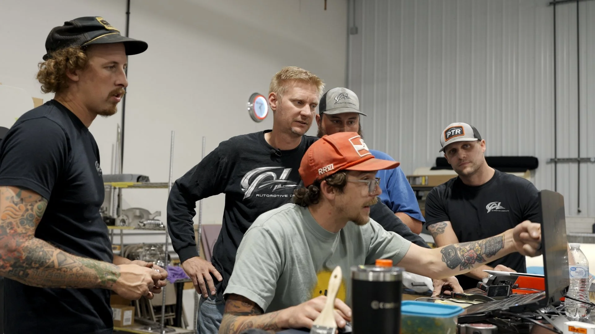 Custom car builders at CAL Auto Creations collaborating on fabrication strategy during Barrett-Jackson Cup competition prep.