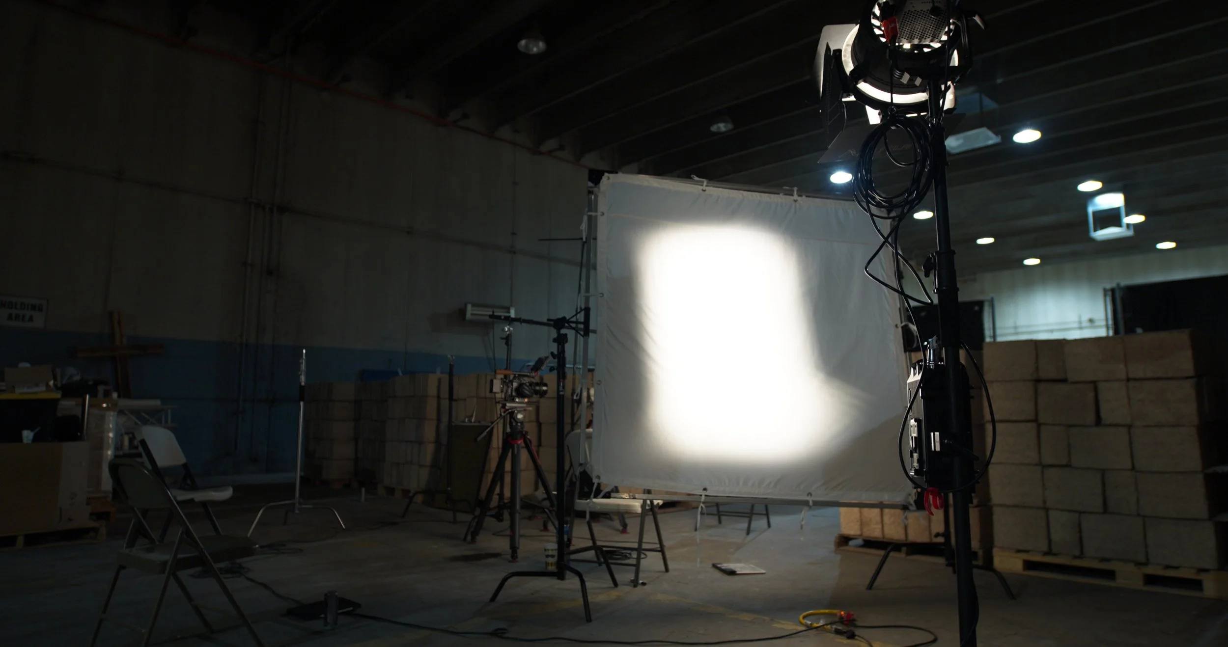 Photography studio setup with a white backdrop, lighting equipment, and cameras in an industrial space with stacked bricks in the background.