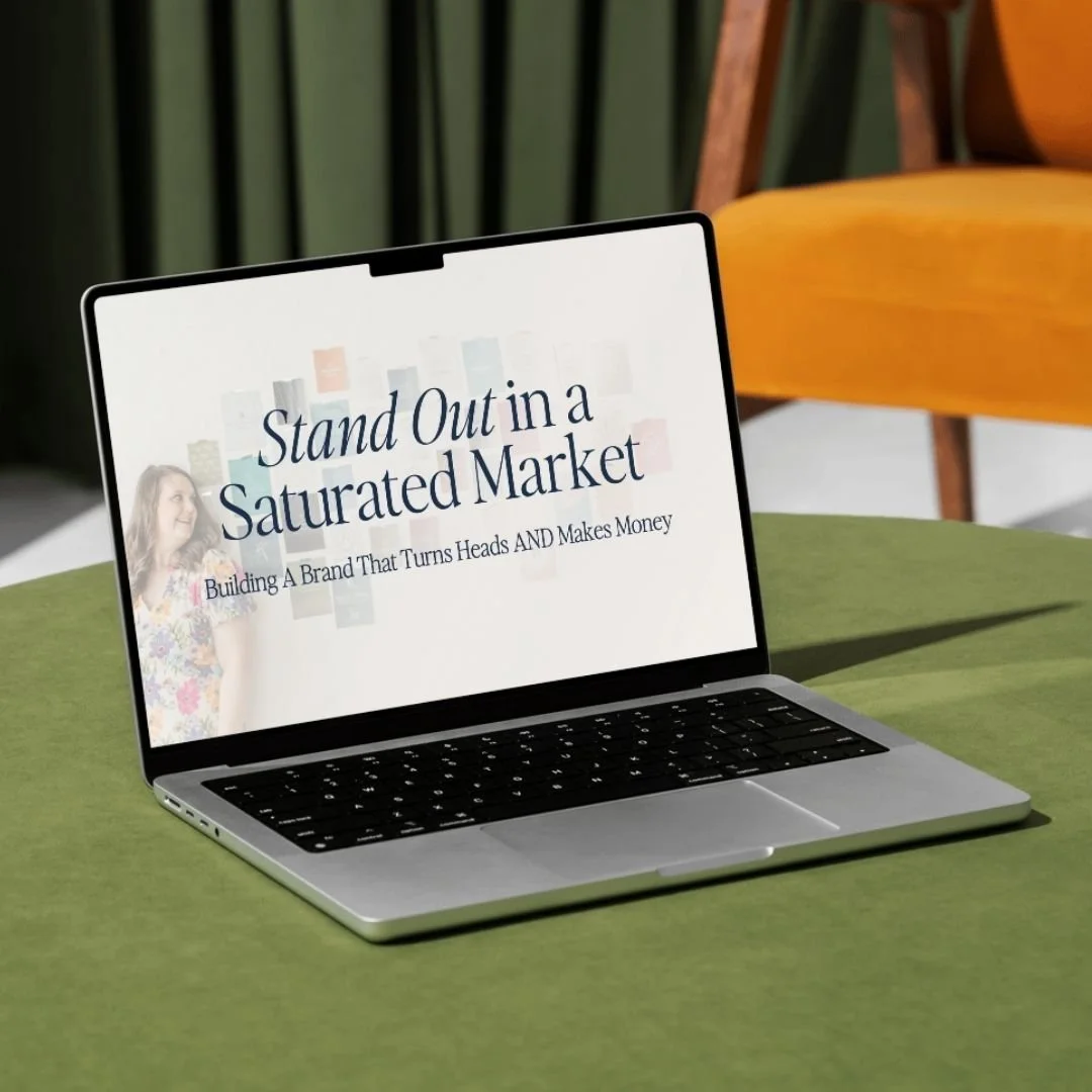 Laptop on a green table displaying a presentation slide that reads "Stand Out in a Saturated Market" with a subtitle "Building A Brand That Turns Heads AND Makes Money."