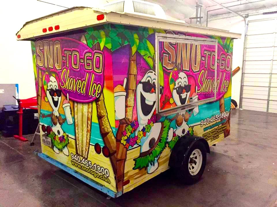 Colorful ice cream food truck with cartoon Olaf from Frozen holding an ice cream cone, advertising shaved ice with a bright and vibrant design in a warehouse.