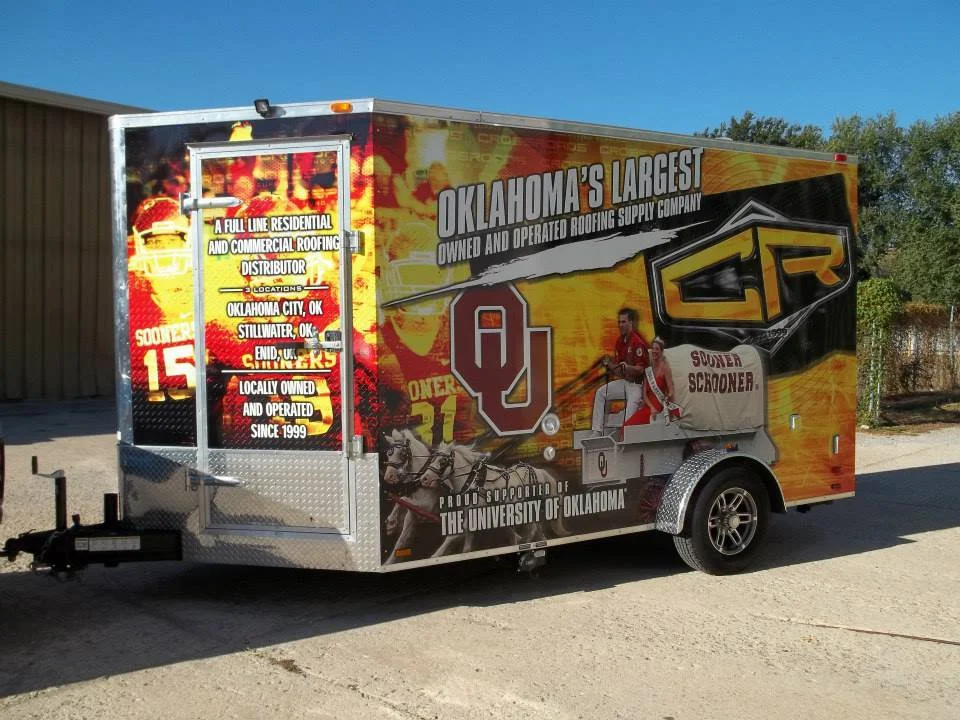 A trailer advertising Oklahoma's largest roofing supply company, featuring logos of the University of Oklahoma and a Scooper, with text about company history and location in Oklahoma. Crossroads Roofing Supply.