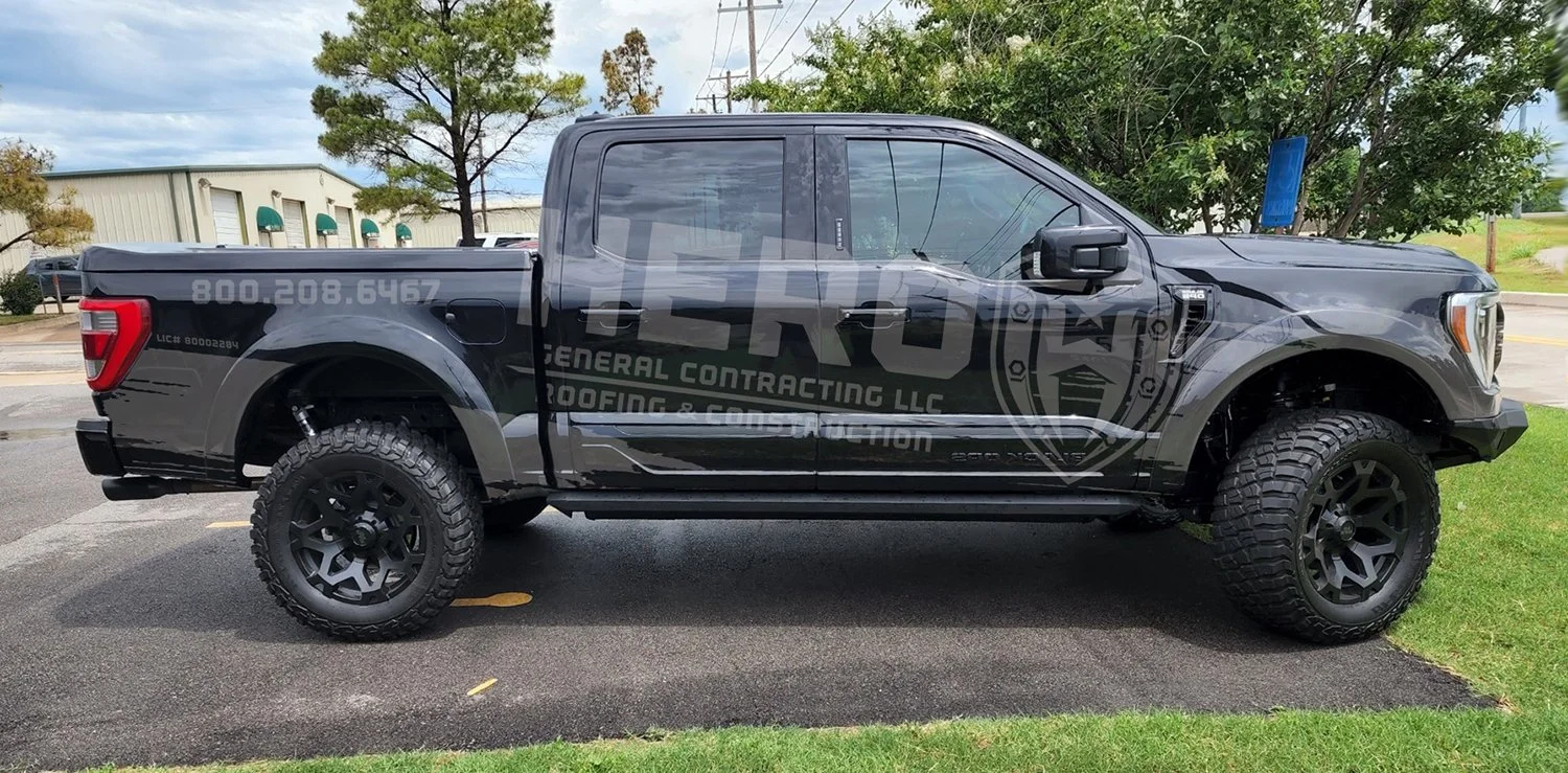 Gray pickup truck with graphic wrap advertising HERO General Contracting LLC parked on a street with trees and buildings nearby.