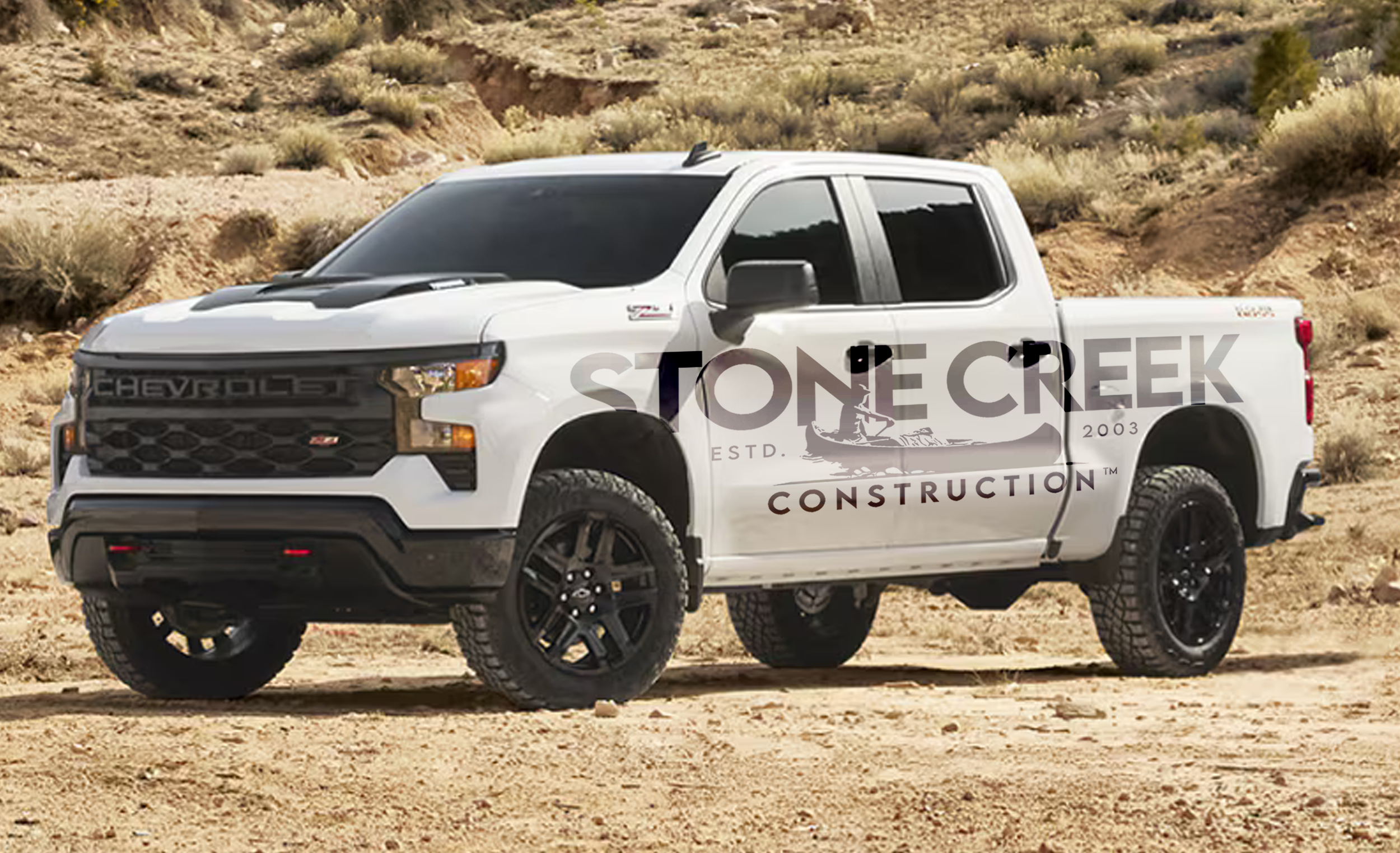 White Chevy truck with Stone Creek Construction logo wrap, parked in a desert landscape.