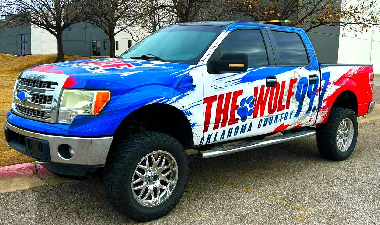 A vehicle wrap of a custom truck with The Wolf Radio Station mascot branding in red, white, and blue.
