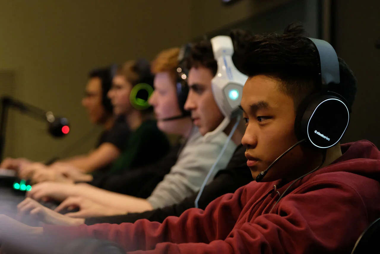 A group of young men wearing headphones, focused on their screens at an esports tournament.