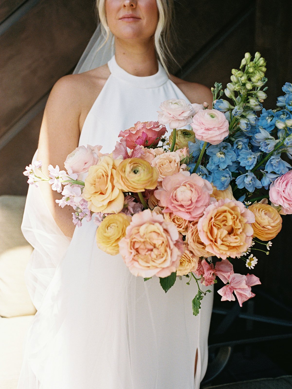 A woman in a white dress holding a large bouquet of pink, peach, and blue flowers.