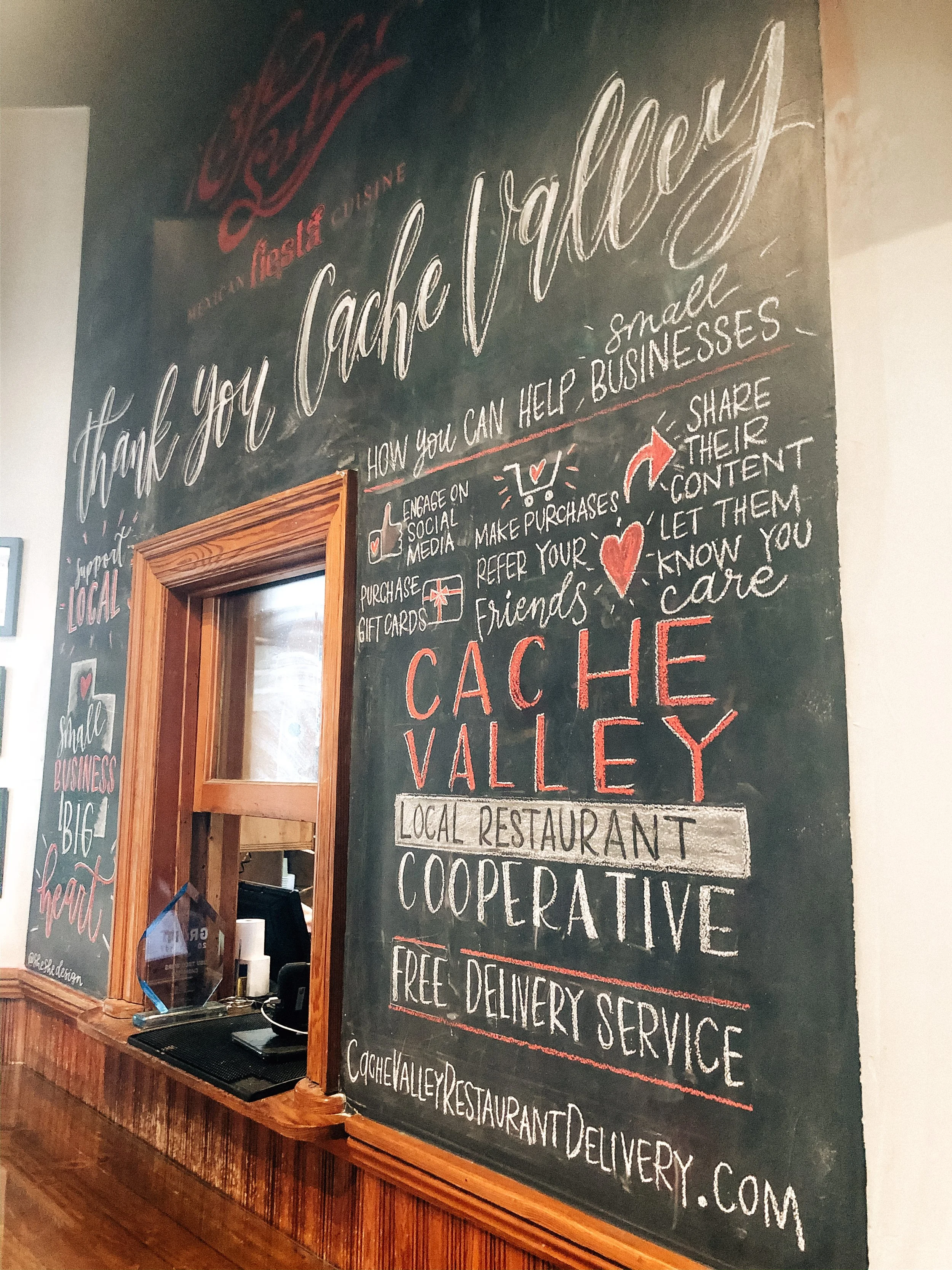 Chalkboard sign promoting Cache Valley, a local restaurant cooperative, with messages about helping small businesses, sharing content, and details about free delivery service.
