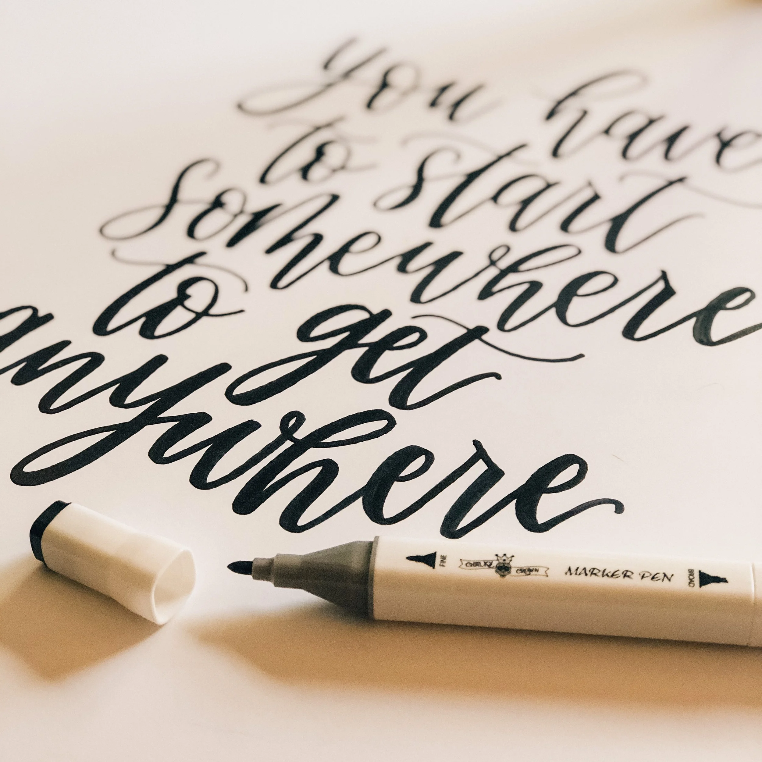 Close-up of black handwritten calligraphy on white paper with a black marker pen and white marker pen cap in the foreground.