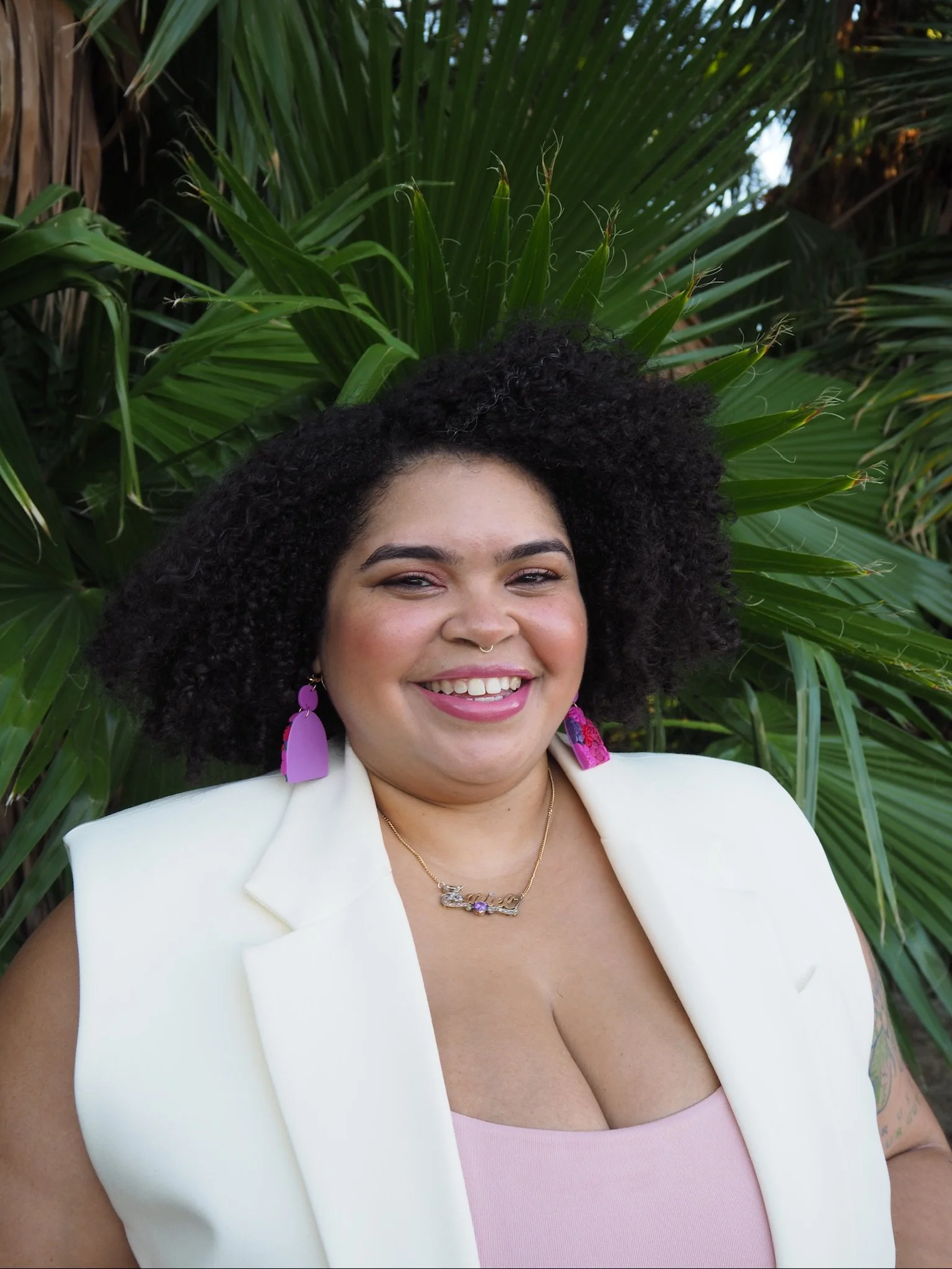 A headshot of Zariel Grullón, a Caribbean woman with light brown skin and curly hair. She is wearing a beige blazer and a pink tanktop.