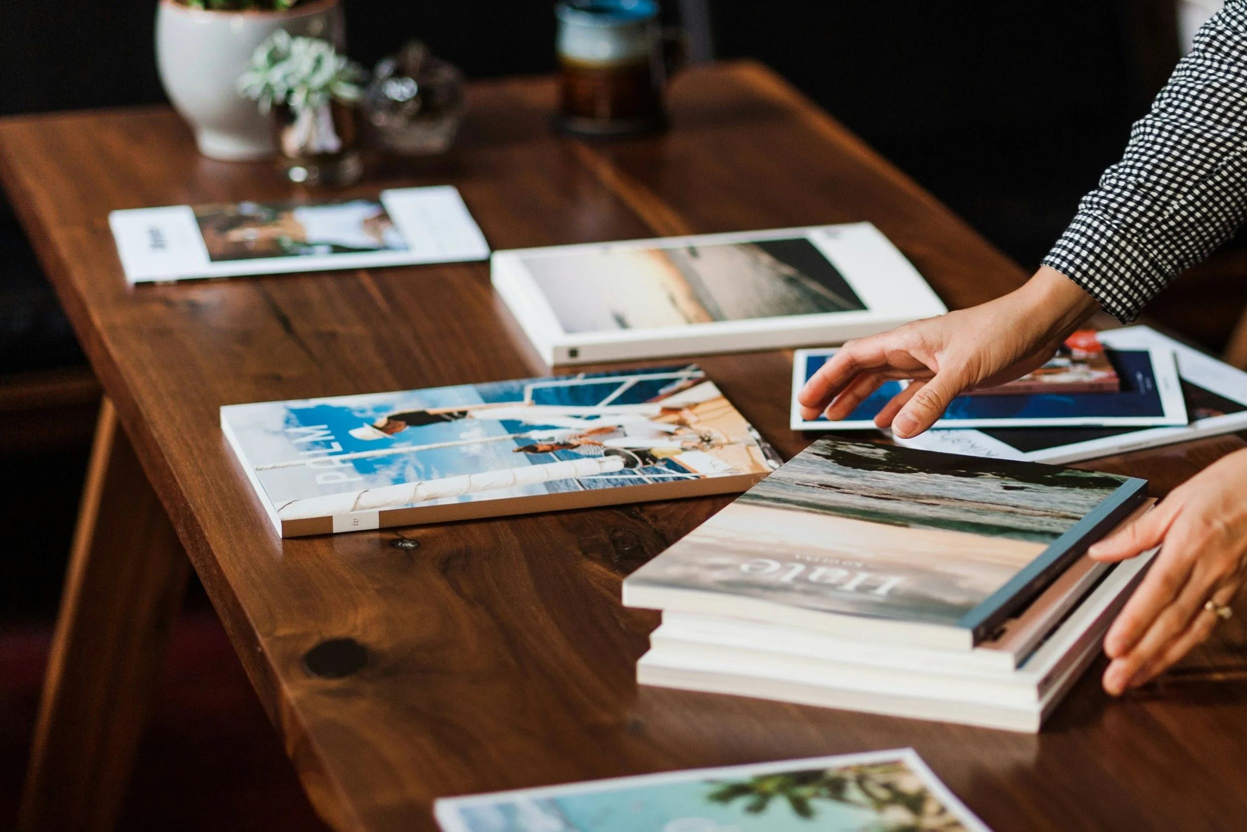[Accessibility description: A photo of a wooden table with various magazines laid out on it and a pair of hands straightening them.]