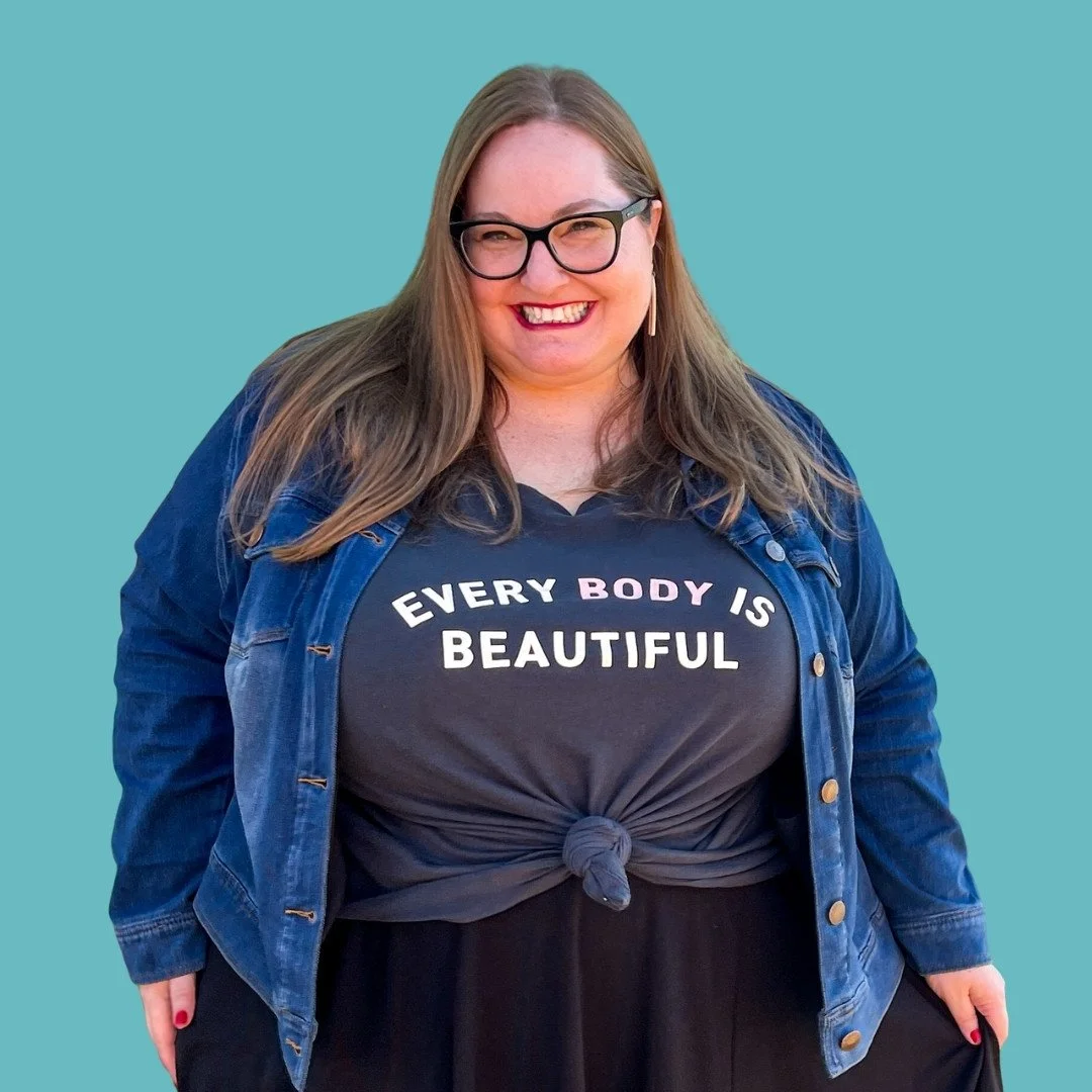 A headshot of Jen McLellan, a plus-size white woman with long light brown hair and black-framed glasses. She is smiling and wearing a denim jacket over a gray shirt that reads, "EVERY BODY IS BEAUTIFUL."