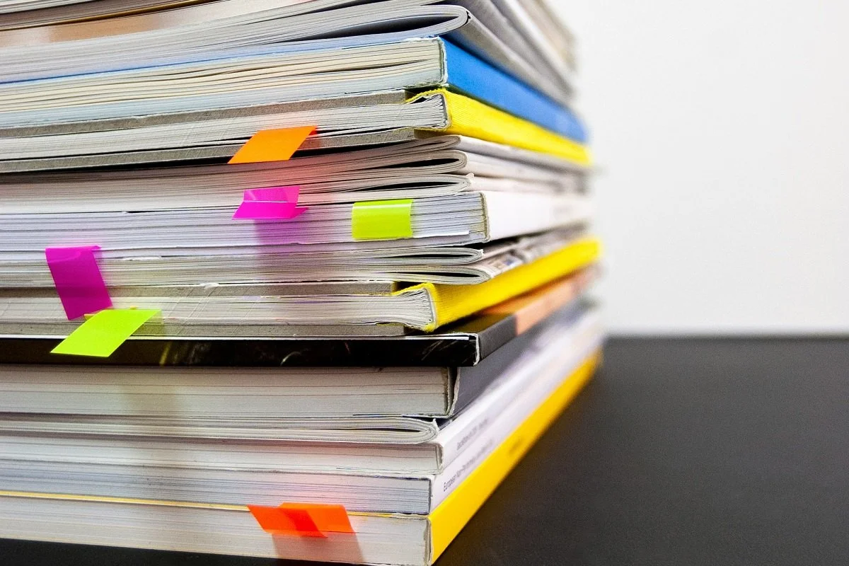 [Accessibility description: A photo of a stack of magazines and books with various colorful page markers sticking out at various points.]