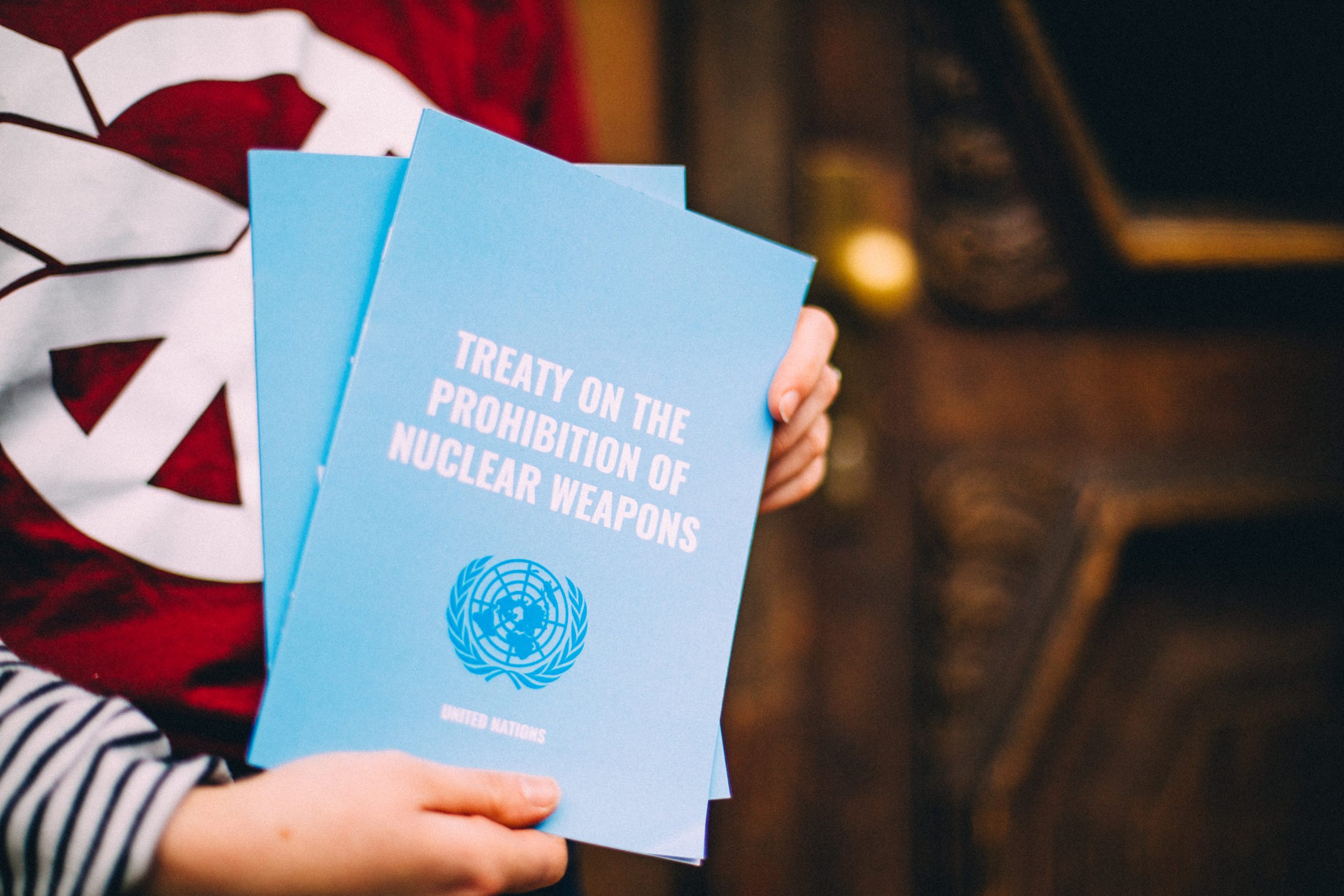 Person holding blue pamphlets about the treaty on the prohibition of nuclear weapons, with the United Nations logo on the cover.