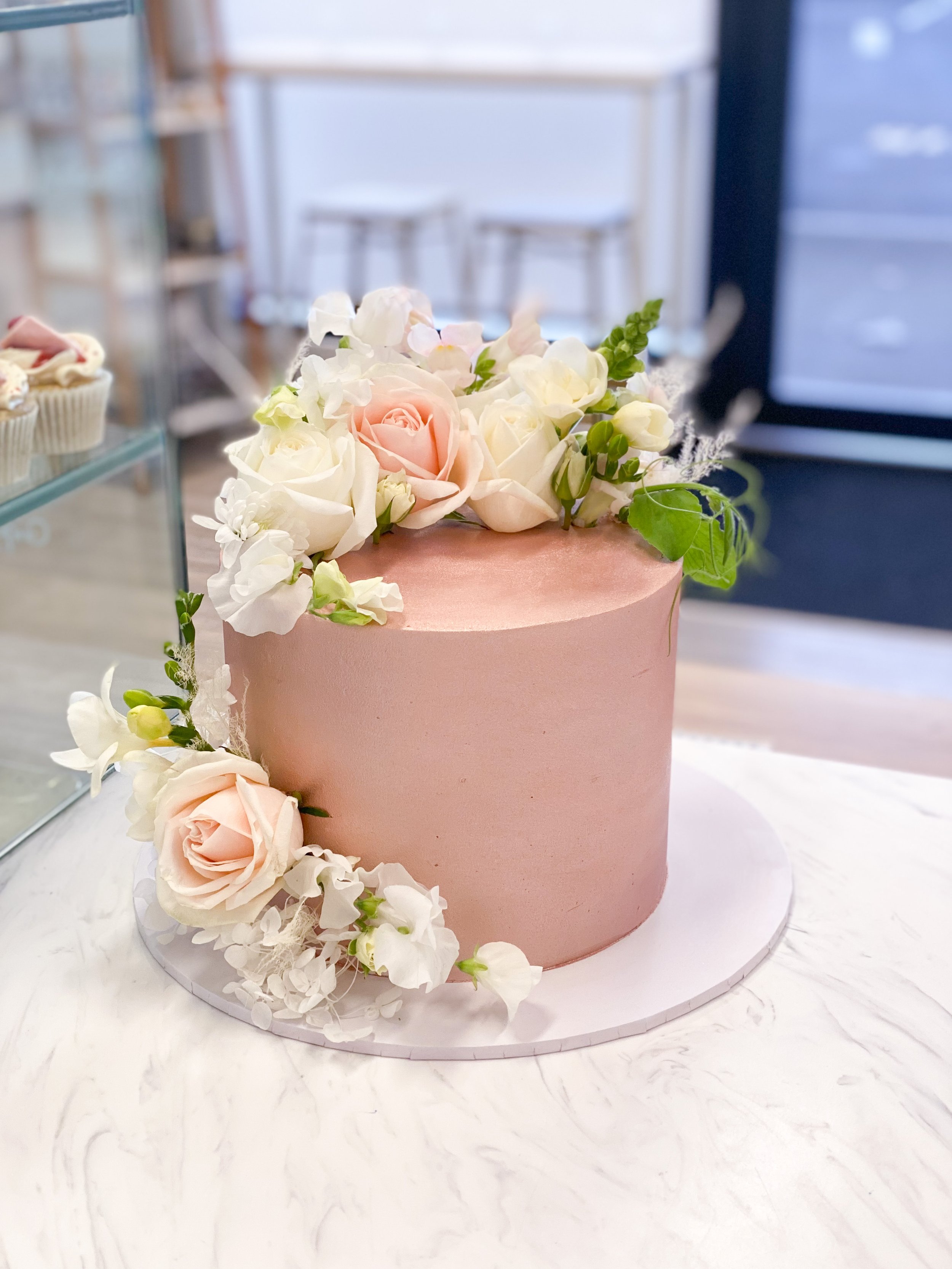Pink cake with white and light pink roses on top, displayed on a marble surface.