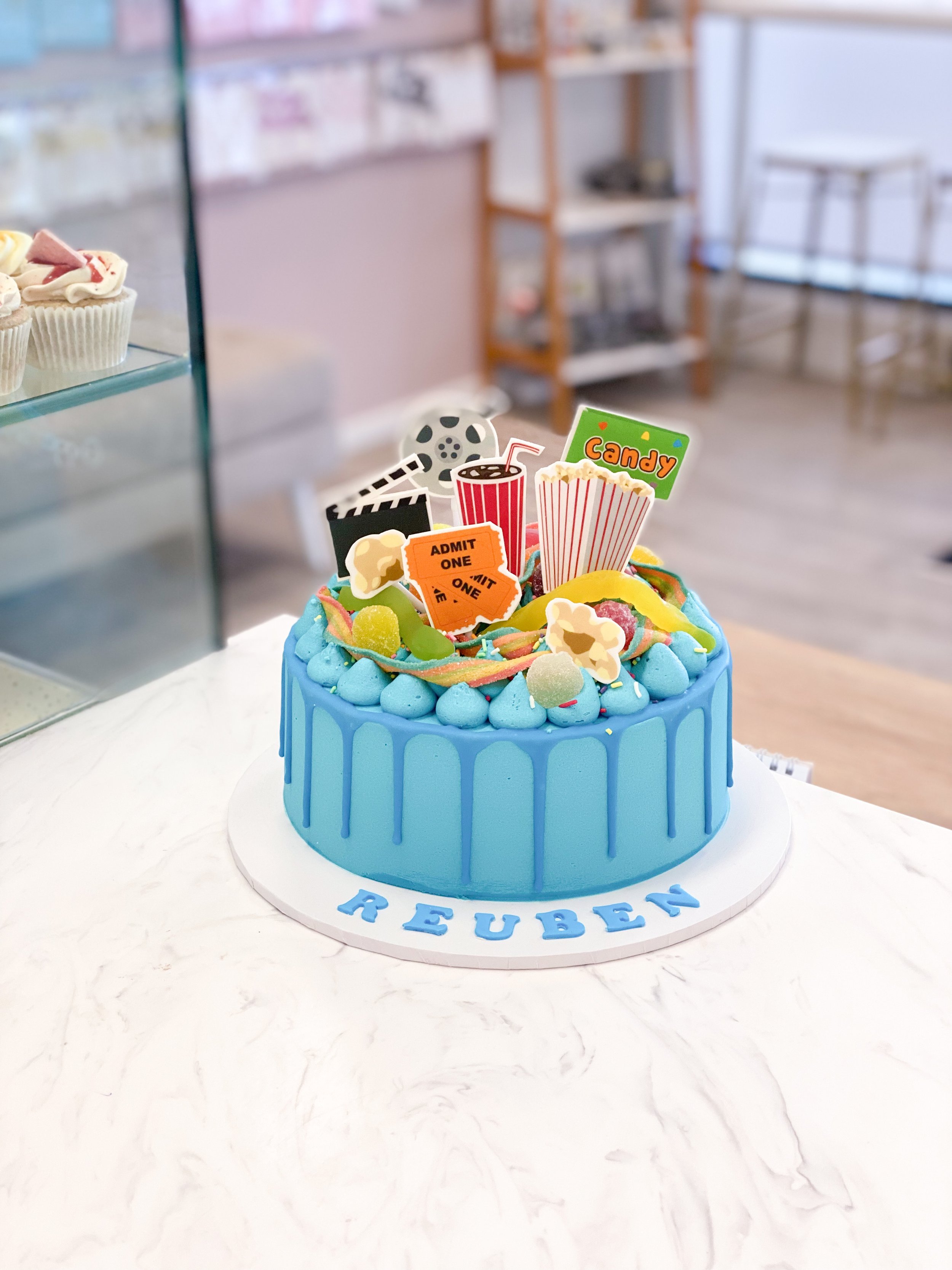 Blue birthday cake with movie-themed decorations including popcorn, candy, a film reel, and a clapperboard on top.