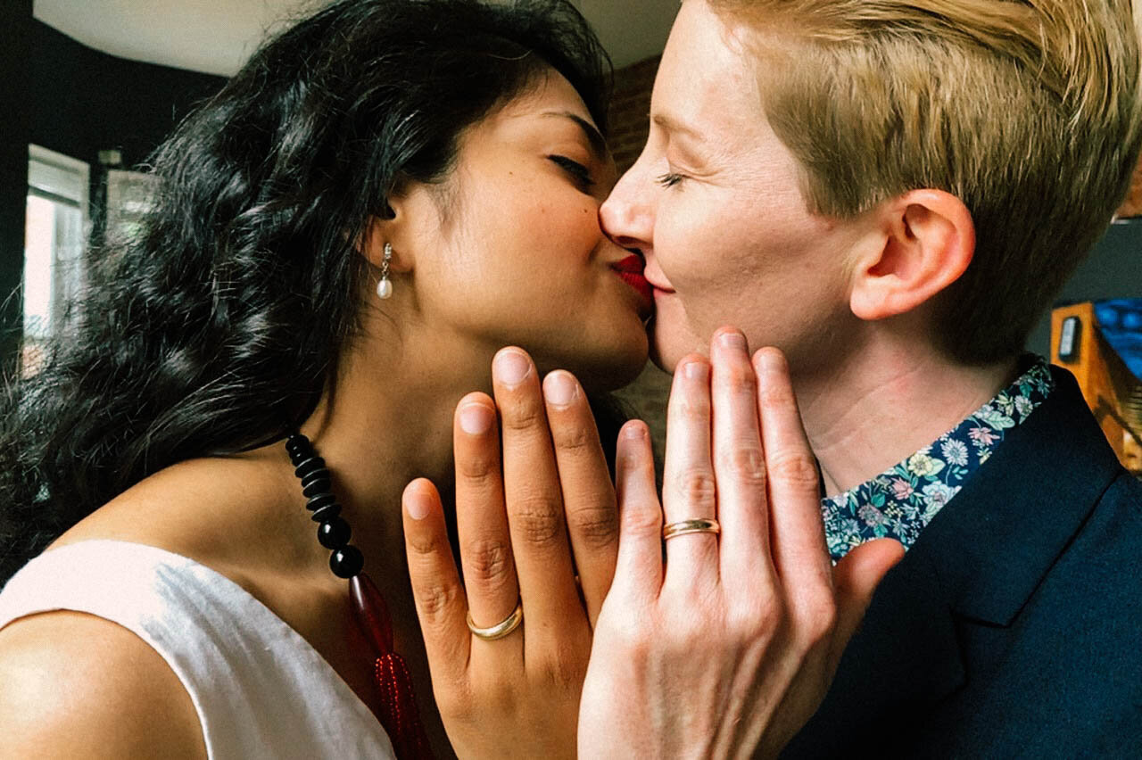 Newlyweds kissing and holding up their wedding ring clad hands in DC Shawnee Custalow Queer Wedding Photographer