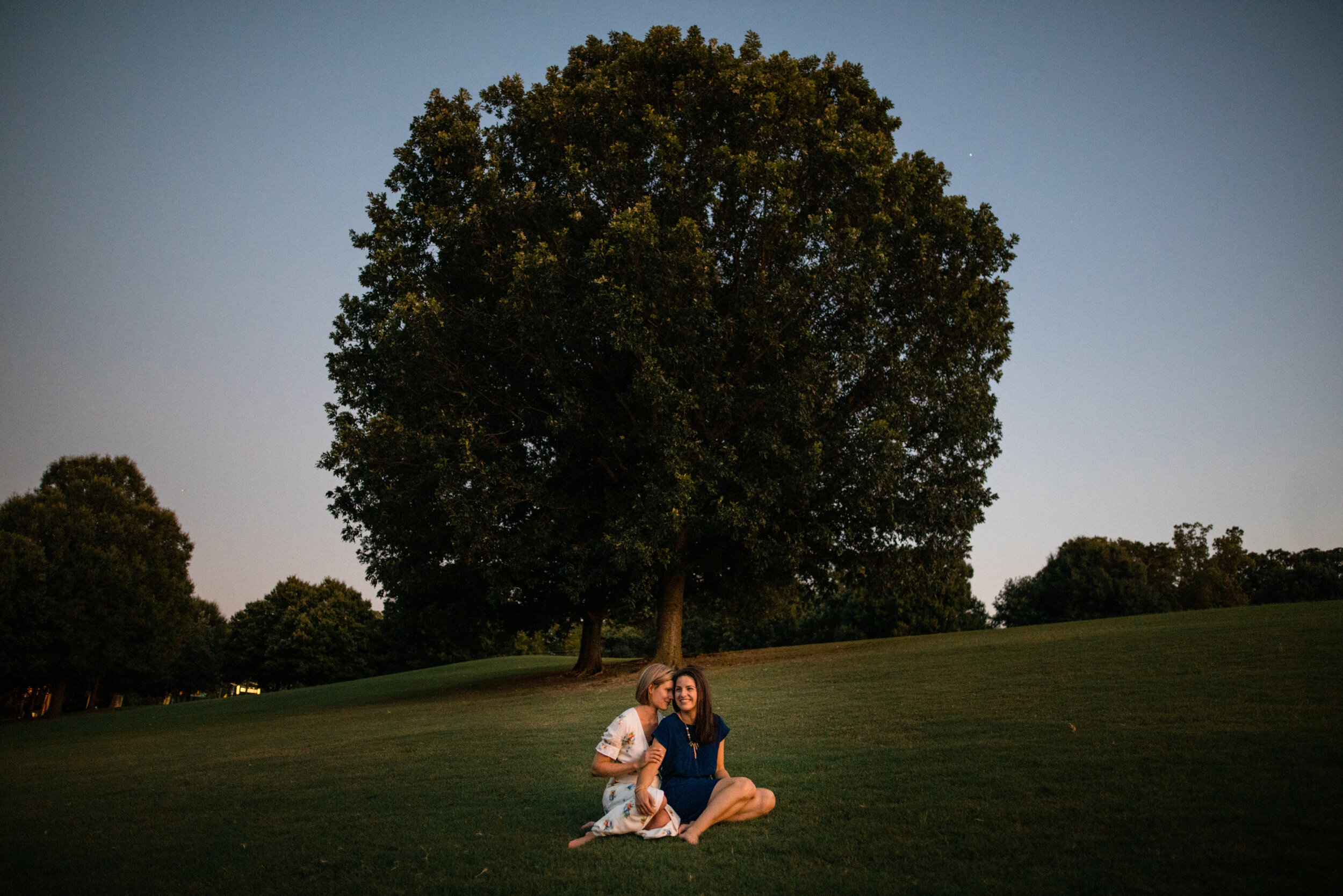 LGBTQ couple sitting together on a grassy field in Richmond VA Shawnee Custalow Queer Wedding Photographer