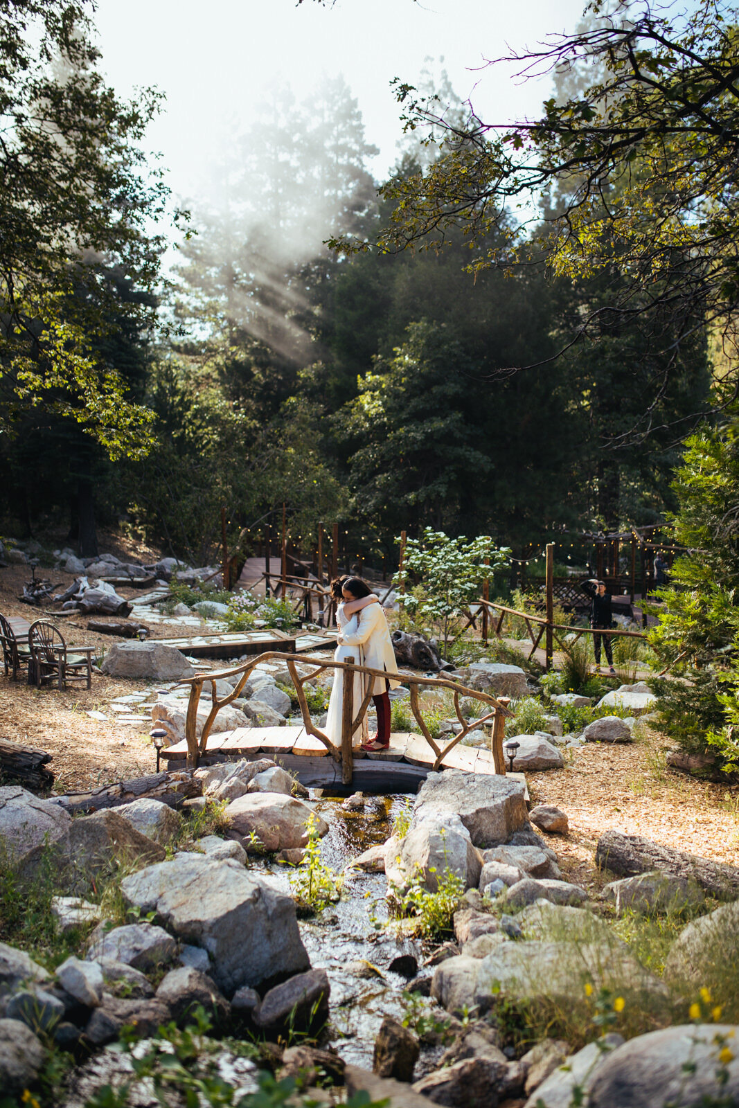 Newlywed couple embracing on a small bridge over a creek in a landscaped garden RVA Shawnee Custalow Queer Wedding Photographer