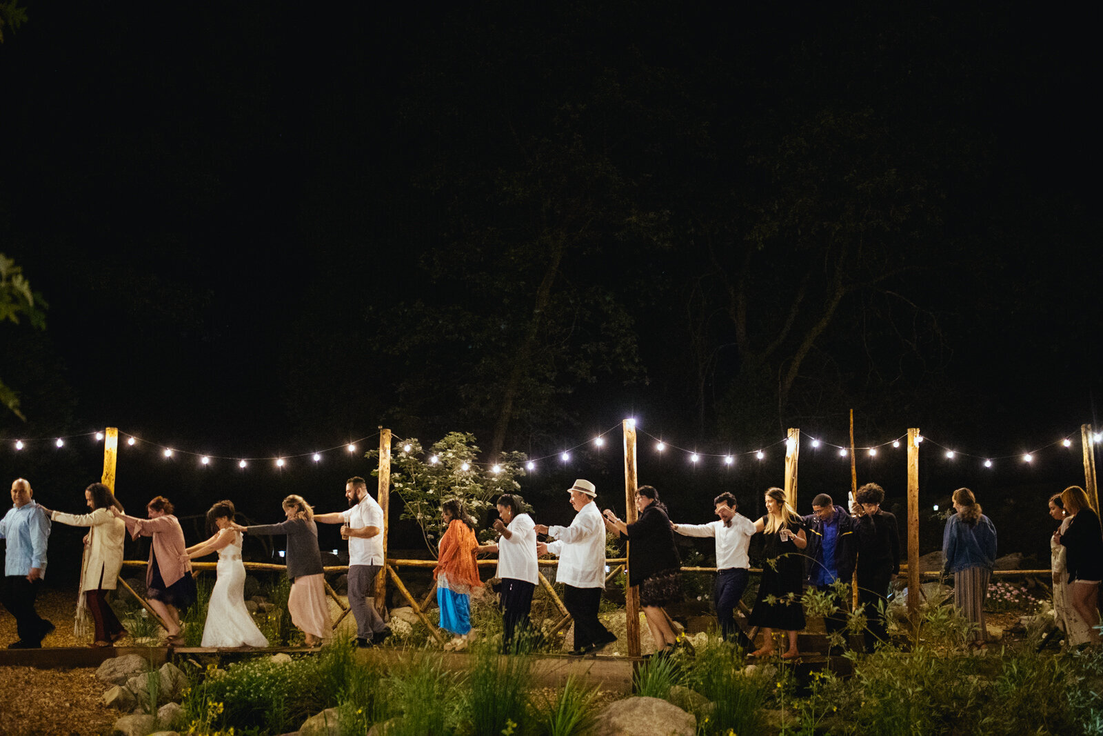 Wedding party in a conga line in a landscaped garden in Richmond VA Shawnee Custalow Queer Wedding Photographer