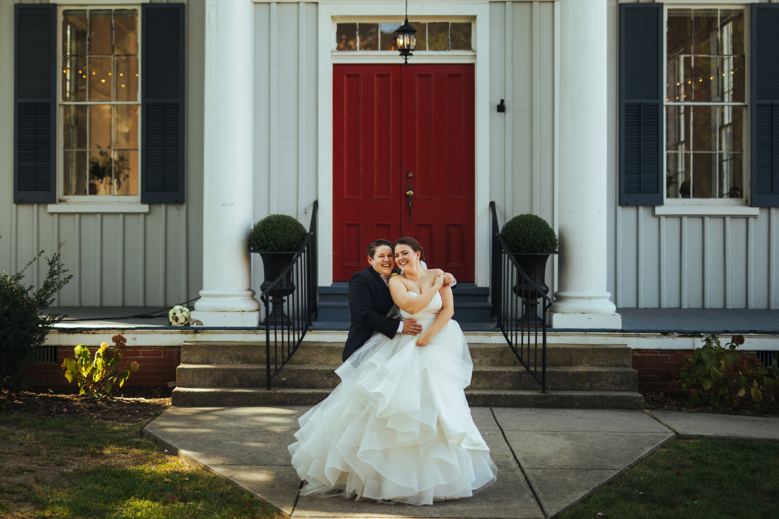 LGBTQ married couple holding each other in front of a large southern veranda in Richmond VA Shawnee Custalow Queer Wedding Photographer